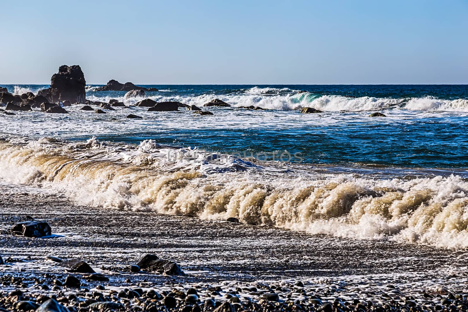 Waves and foam on wild stone beach on shore of the Atlantic ocean with sky and rock on skyline or horizon in Tenerife Canary island, Spain at spring or summer