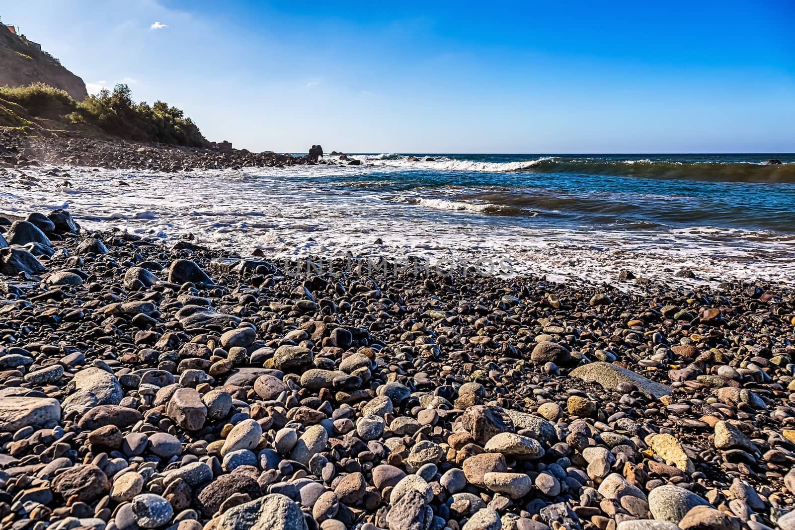 Wild stone beach on coast or shore  of the Atlantic ocean with waves and blue sky and  horizon in Tenerife Canary island, Spain