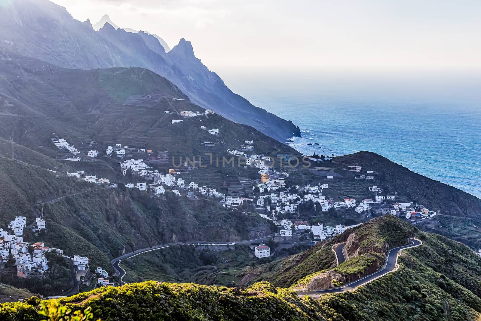 City or village and winding or serpantine road in green mountain or rock valley and clouds with horizon landscape near shore of Atlantic ocean in Tenerife Canary island, Spain