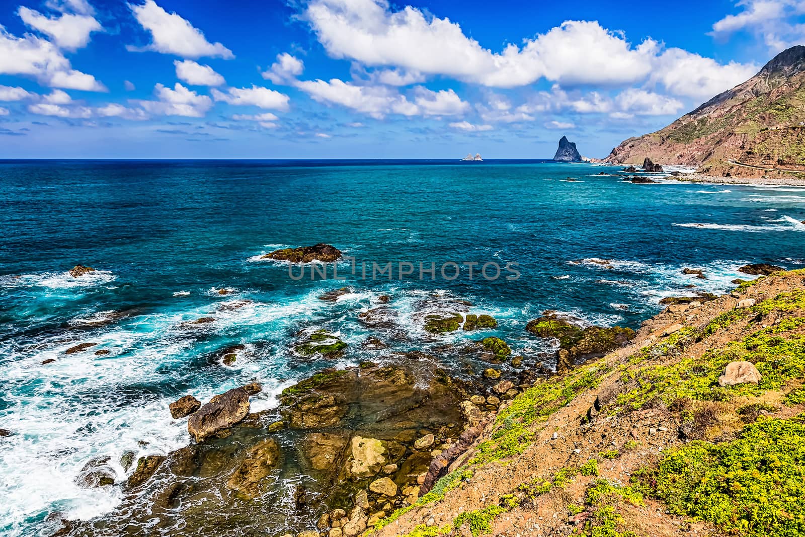 Coast or shore of Atlantic ocean with green mountain or rock and blue sky with clouds and horizon in Tenerife Canary island, Spain at spring or summer
