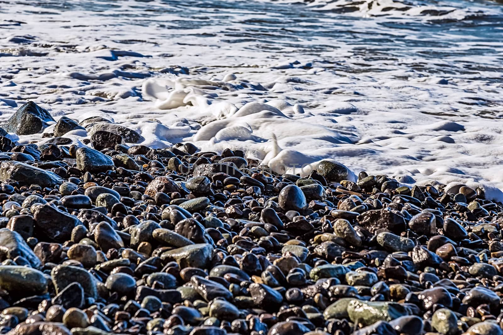 Stones and water with foam and waves on the beach coast or shore of ocean or sea