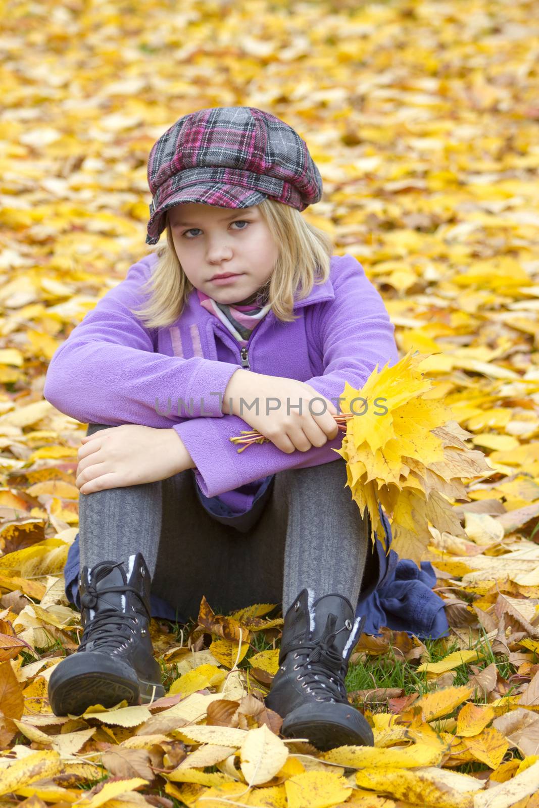 little girl sitting on leaves in the park by miradrozdowski