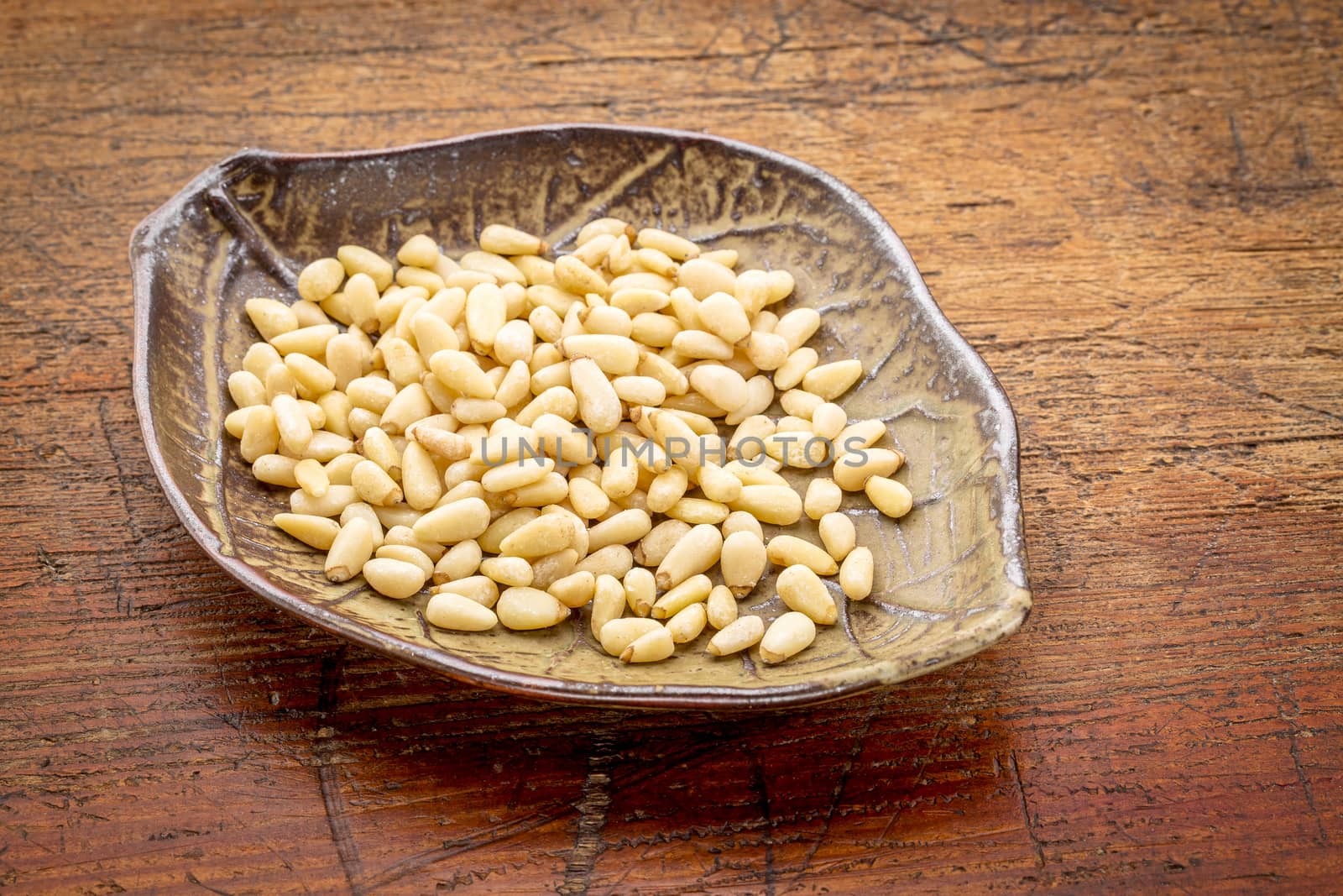 pine nuts on a ceramic, leaf shaped, bowl against rustic grunge wood surface