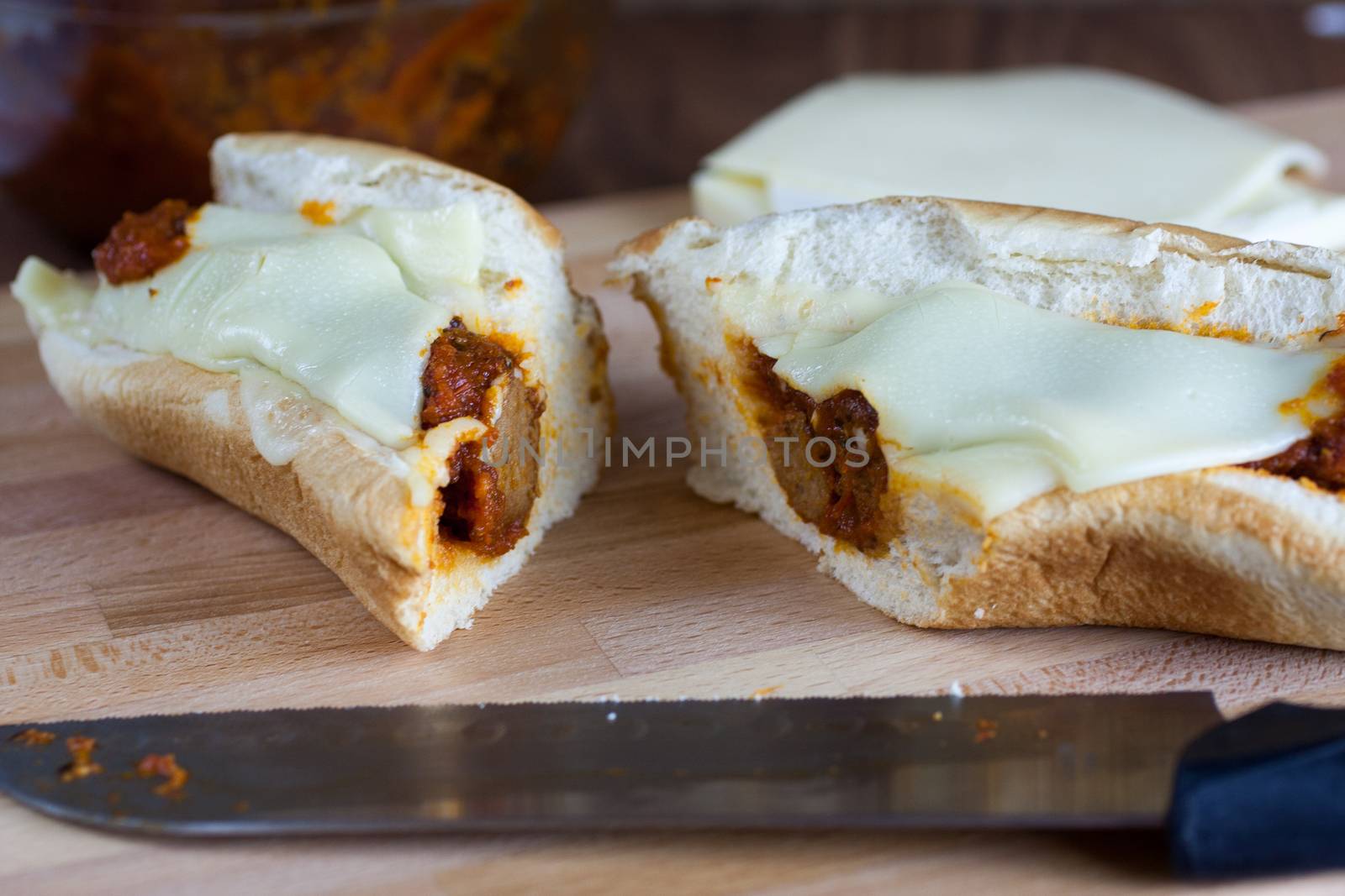 A fresh meatball sandwich with cheese on wooden cutting board.