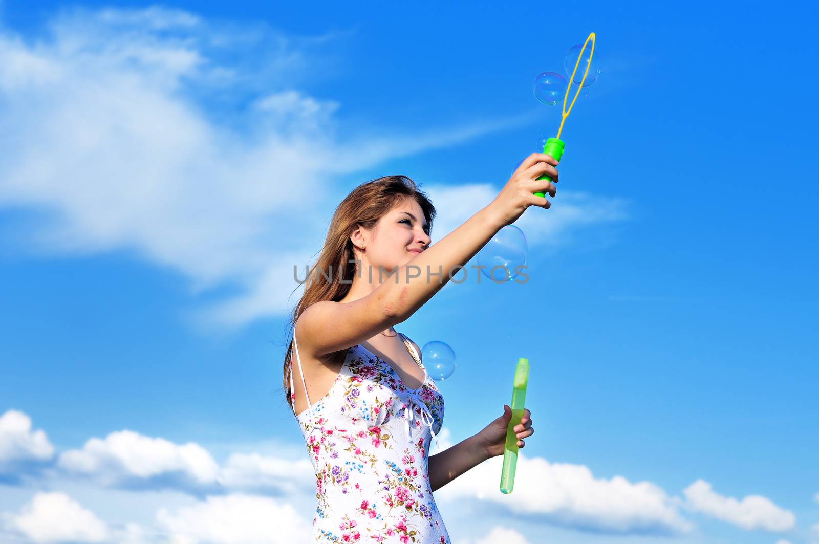 Beautiful teen girl blowing soap bubbles  over blue sky