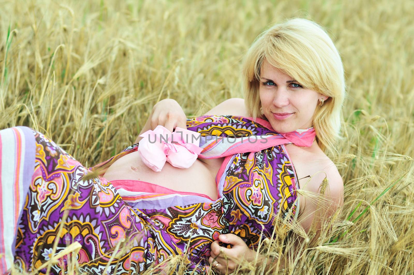pregnant woman laying in wheat field with pink bootee on tummy