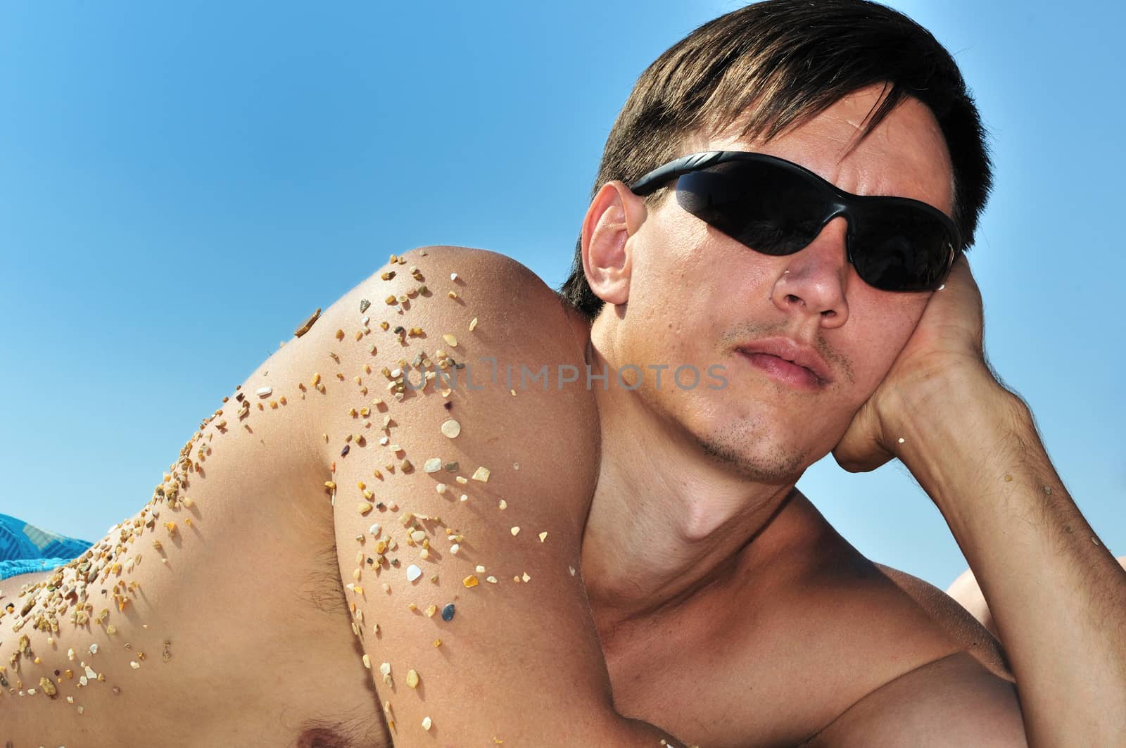 young man wearing sunglasses laying on the beach