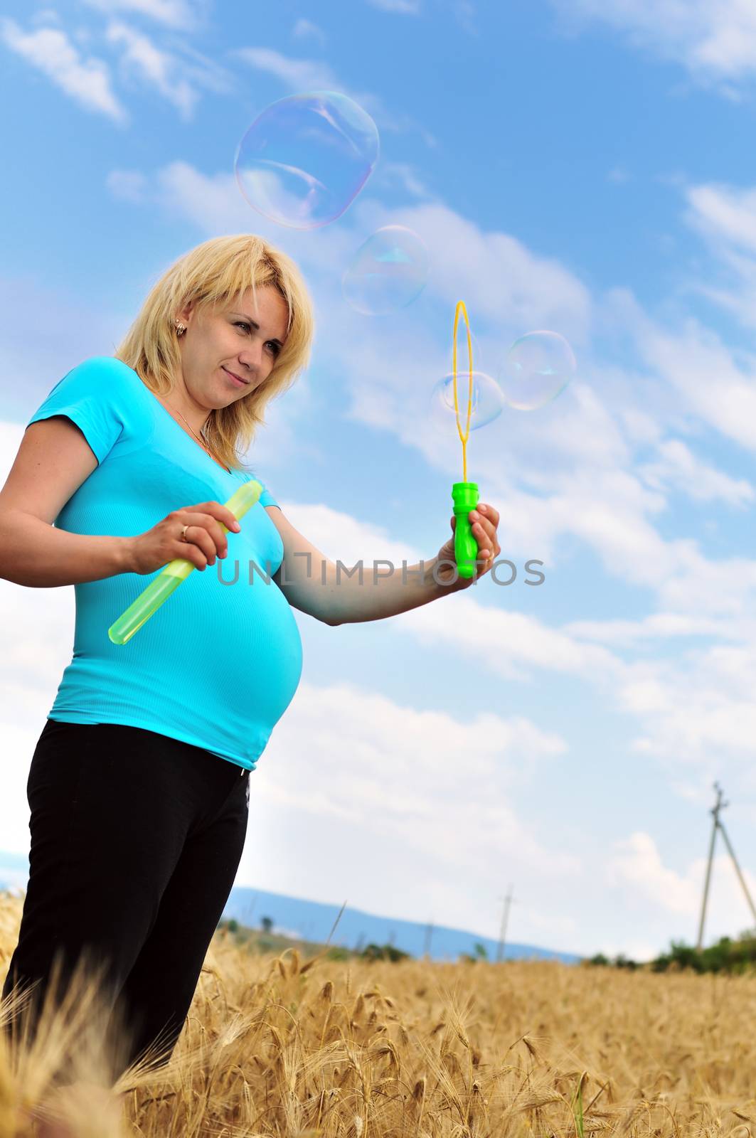 pregnant woman playing with soap bubbles in the wheat field 