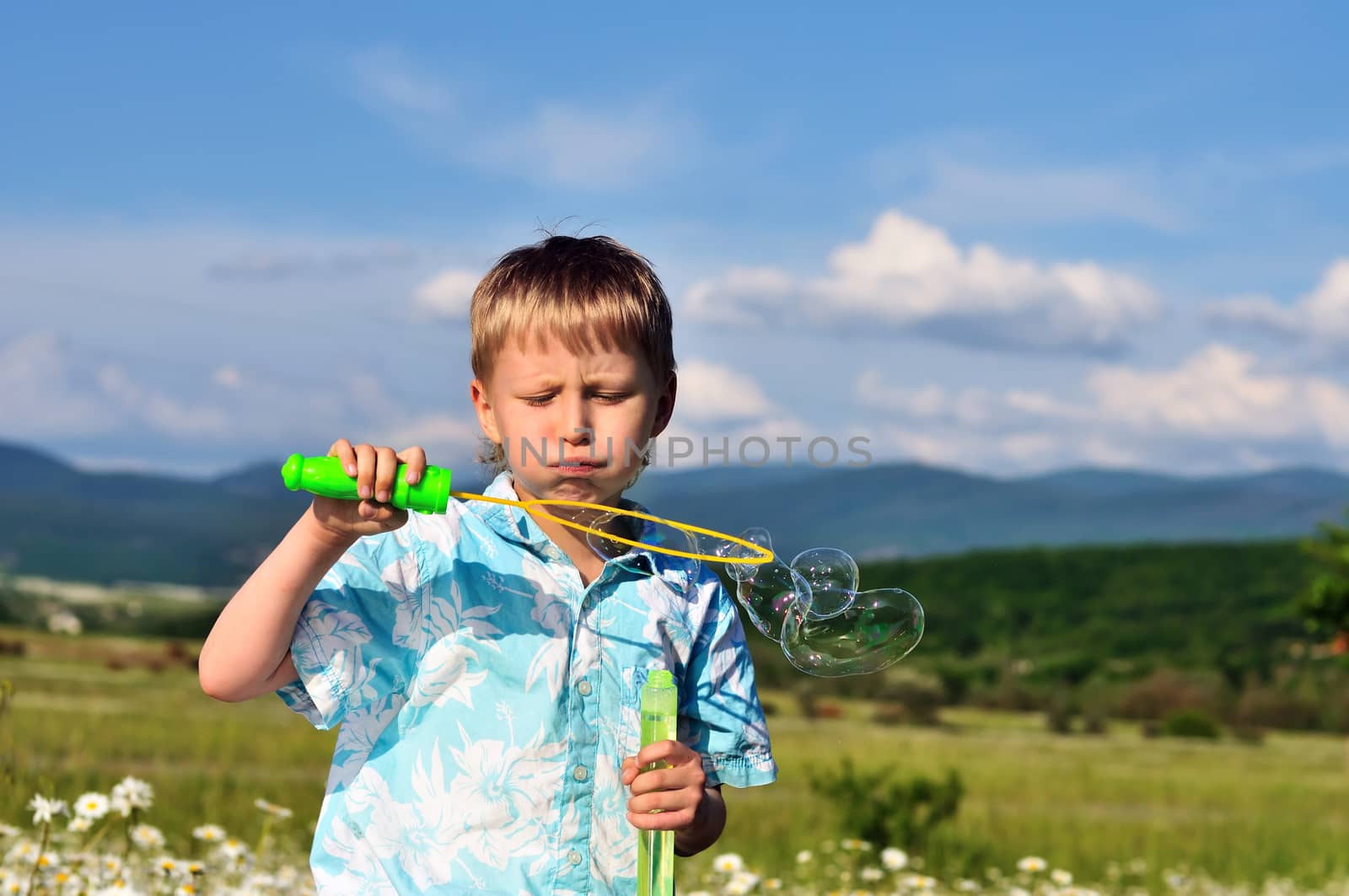 little boy blowing soap bubbles in daisy field