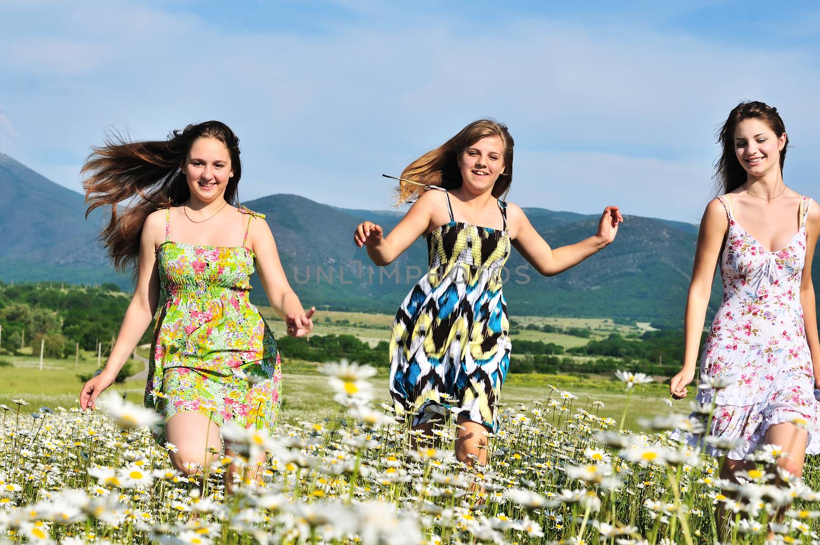 teen happy friends girls running in daisy field in summer day