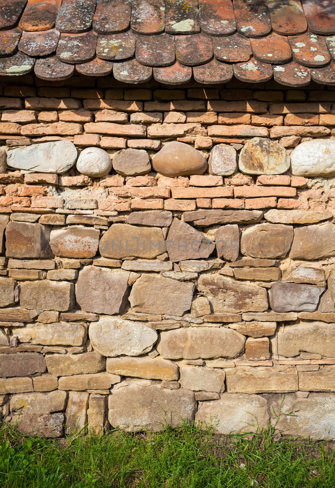 Rustic wall with layers of different comstruction materials - sandstones, bricks, river stones and roof tiles