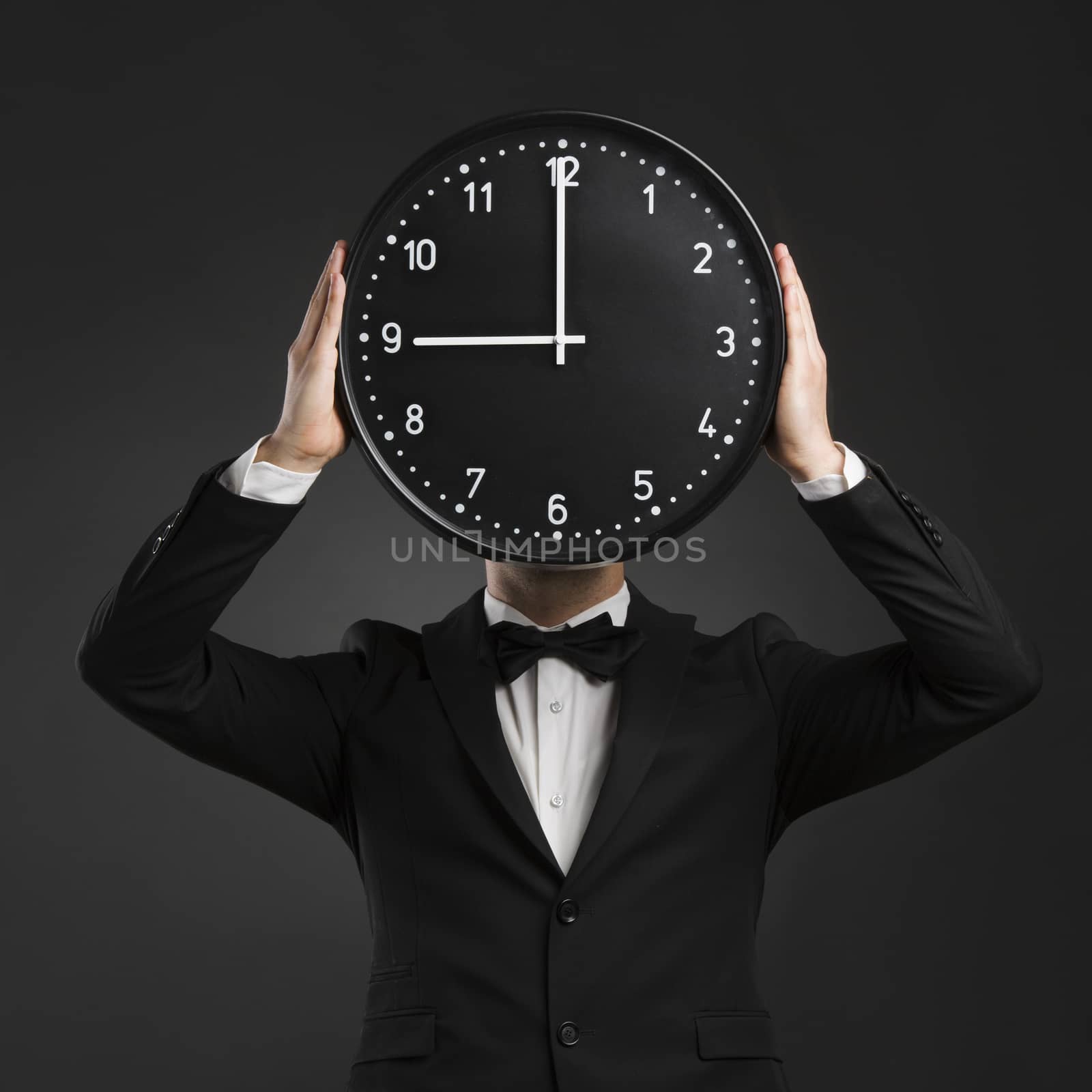 Handsome young man wearing a tuxedo and holding a clock