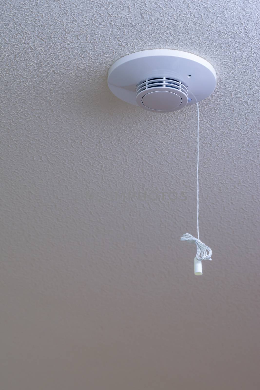 A white fire alarm on a textured white ceiling.