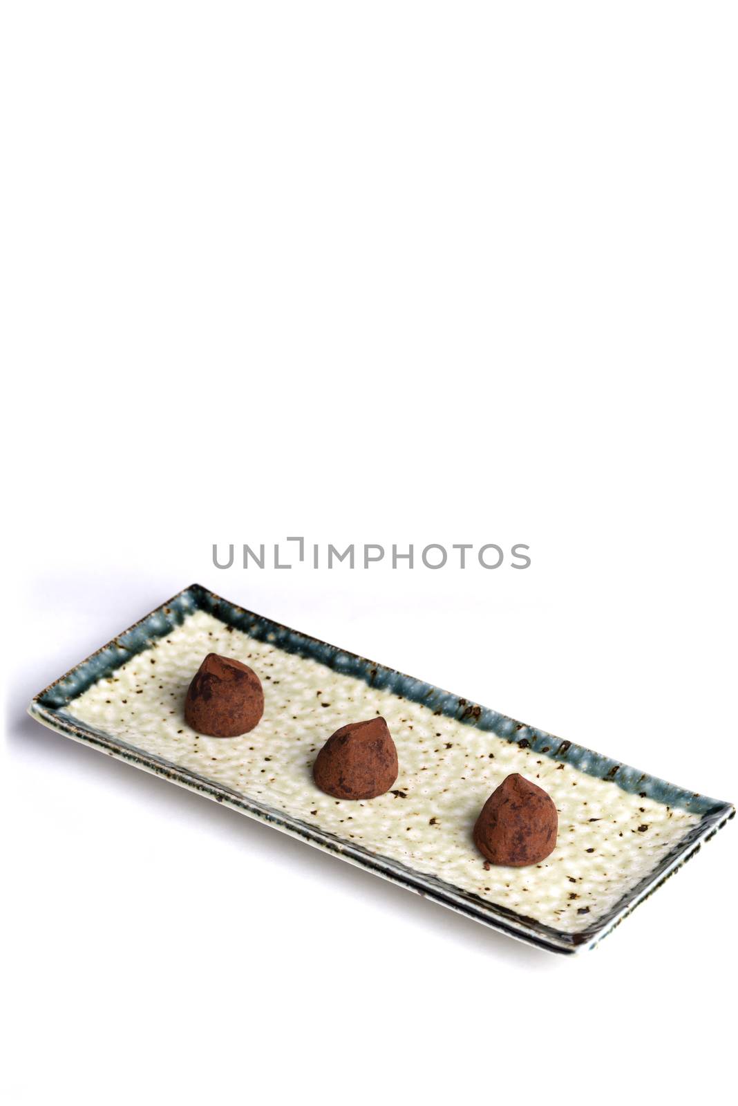Three chocolate truffles on a ceramic plate with a pure white background.