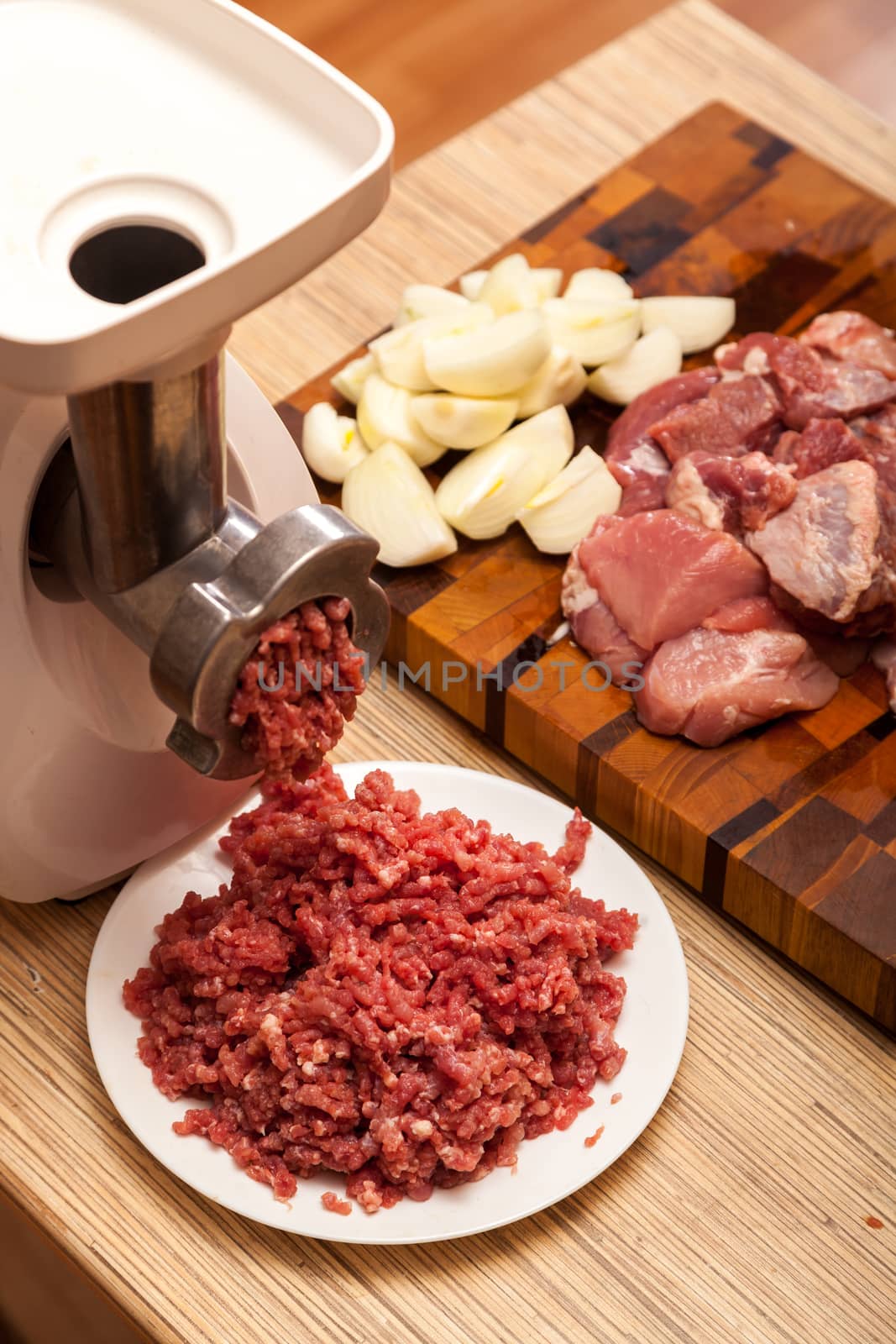 The electric meat grinder, forcemeat, onions and the cut meat on a chopping board