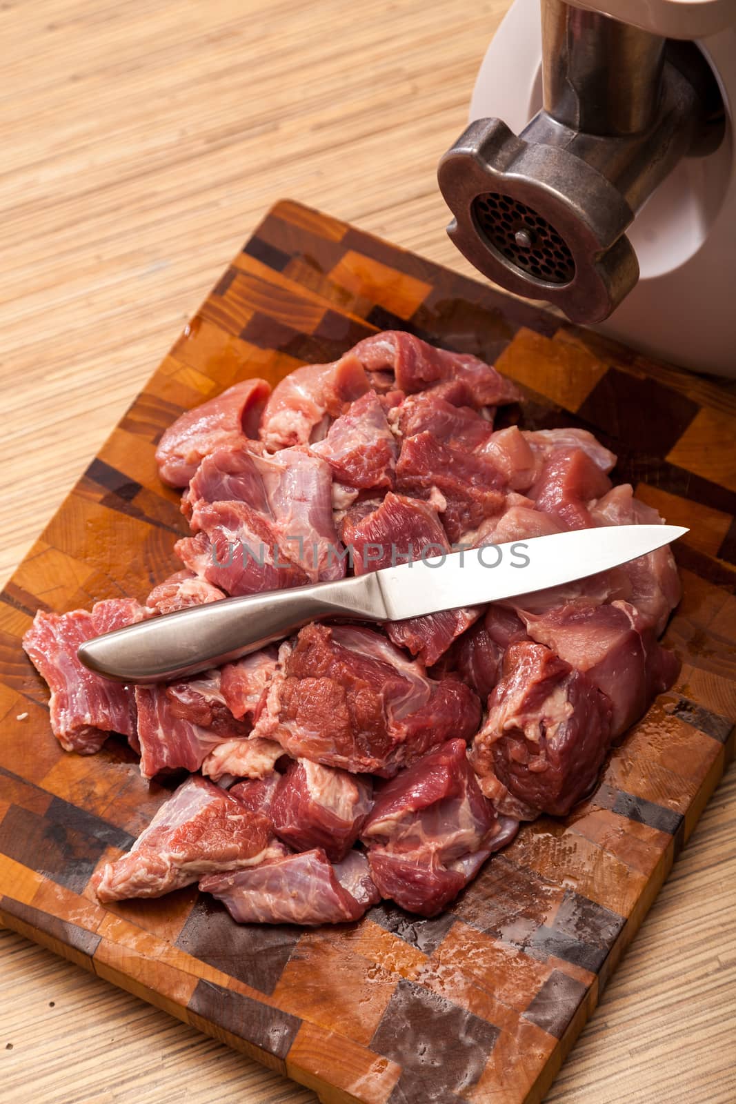 The electric meat grinder and the cut meat on a wooden chopping board