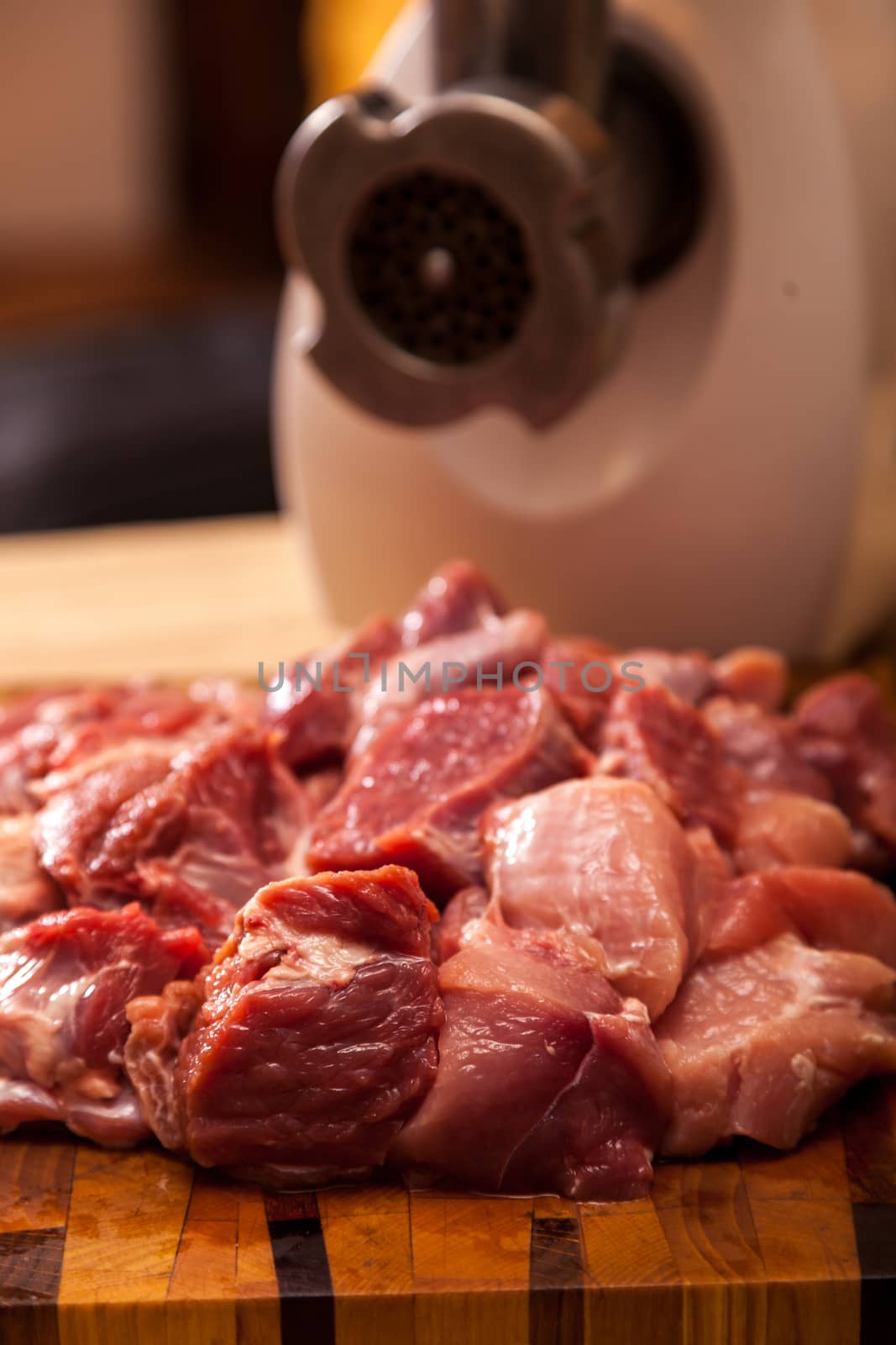 The electric meat grinder and the cut meat on a wooden chopping board