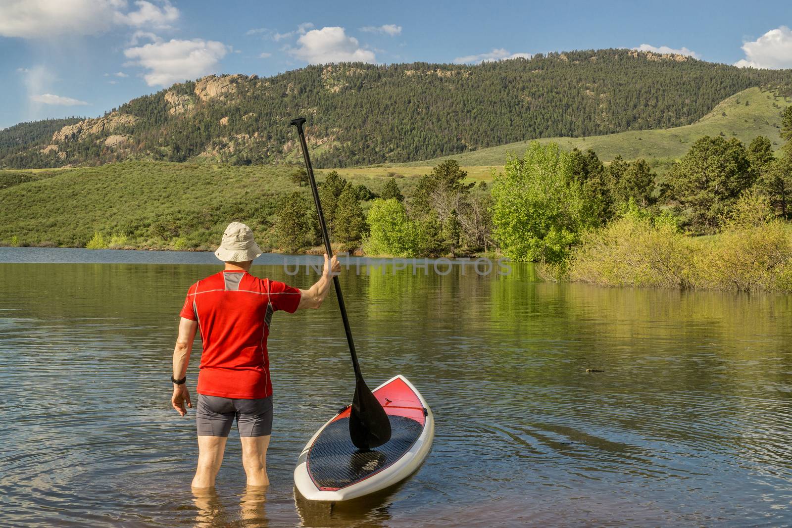 male paddler is about to step on his SUP paddleboard - a shore of Horsetooth Reservoir at foothills of Rocky Mountains, Colorado in early summer