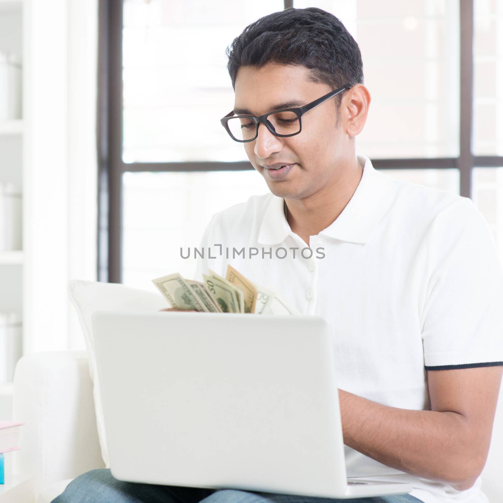Indian guy counting cash, earning money from his successful internet business. Asian man working from home.