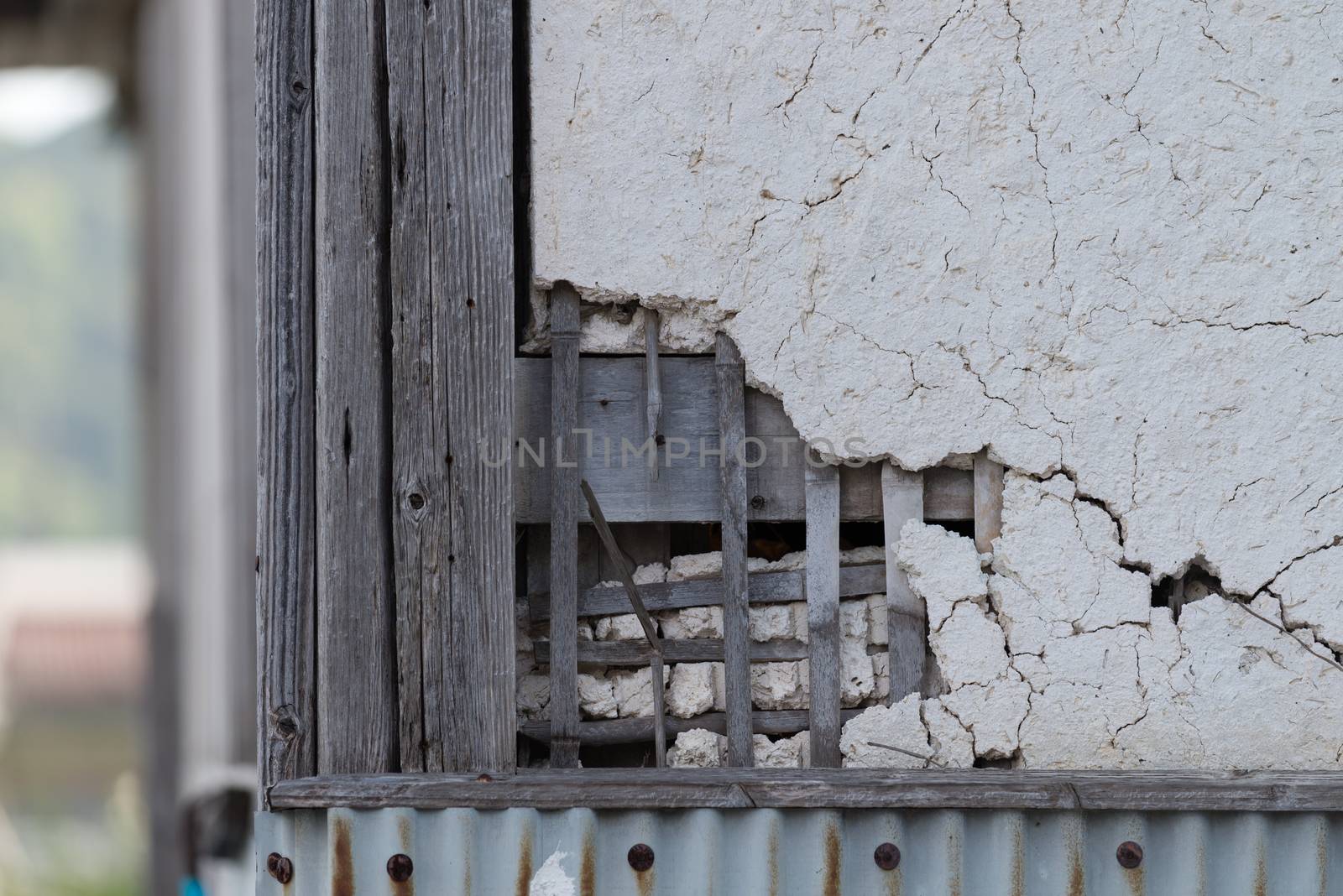 An outdoor old broken and cracked plaster wall with the wooden lattice behind showing through.
