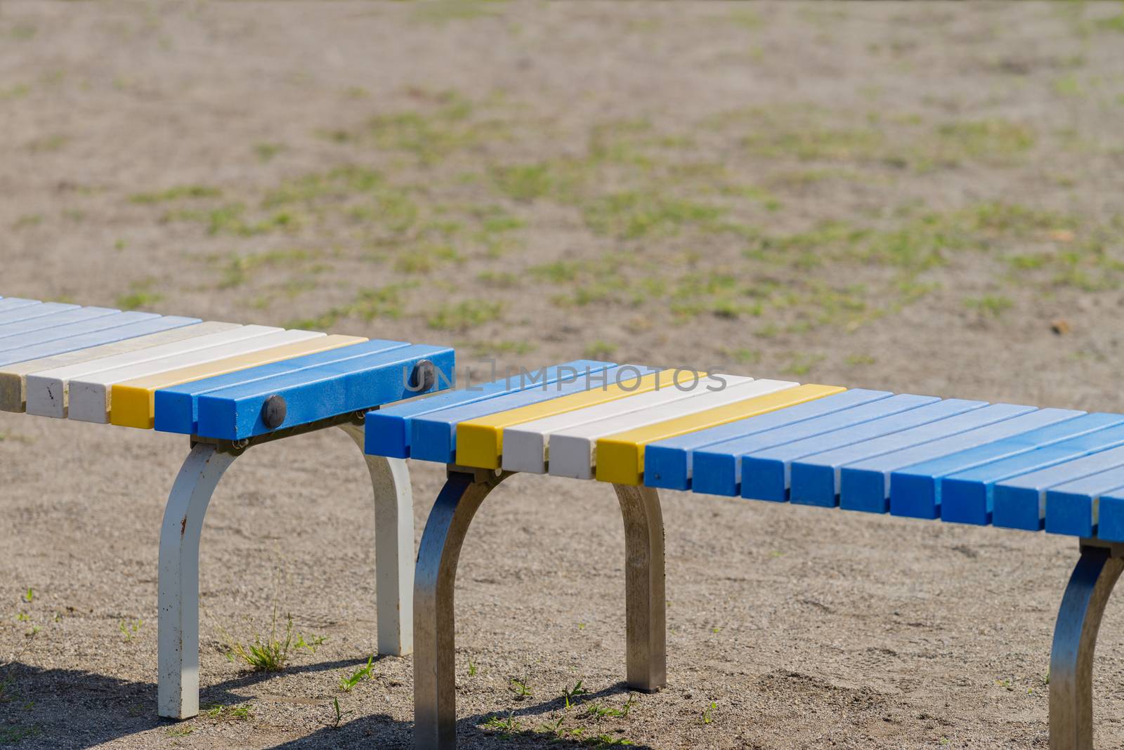 A blue, yellow and white bench on the side of a sports field.