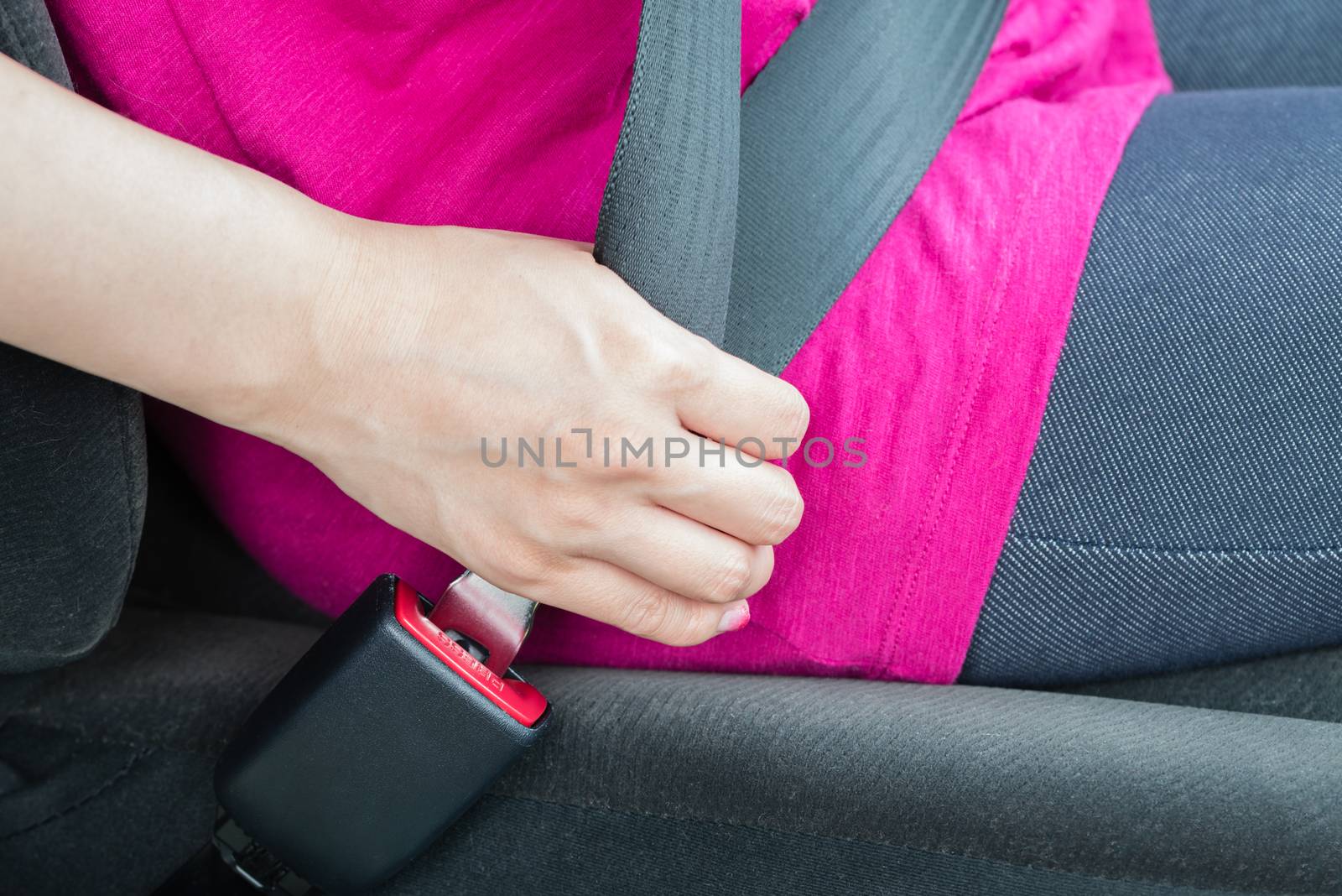 A girl wearing a pink shirt buckling a seatbelt