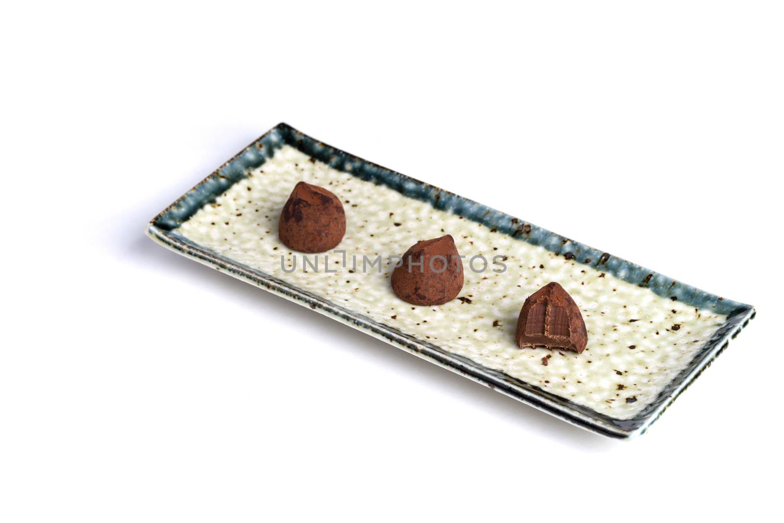 Three chocolate truffles on a ceramic plate with a pure white background. One with a bite taken from it.