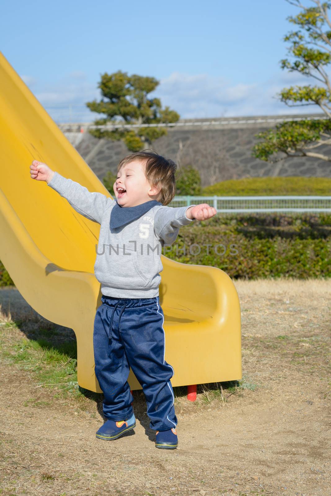 A 2 year old boy celebrating after going down a slide.