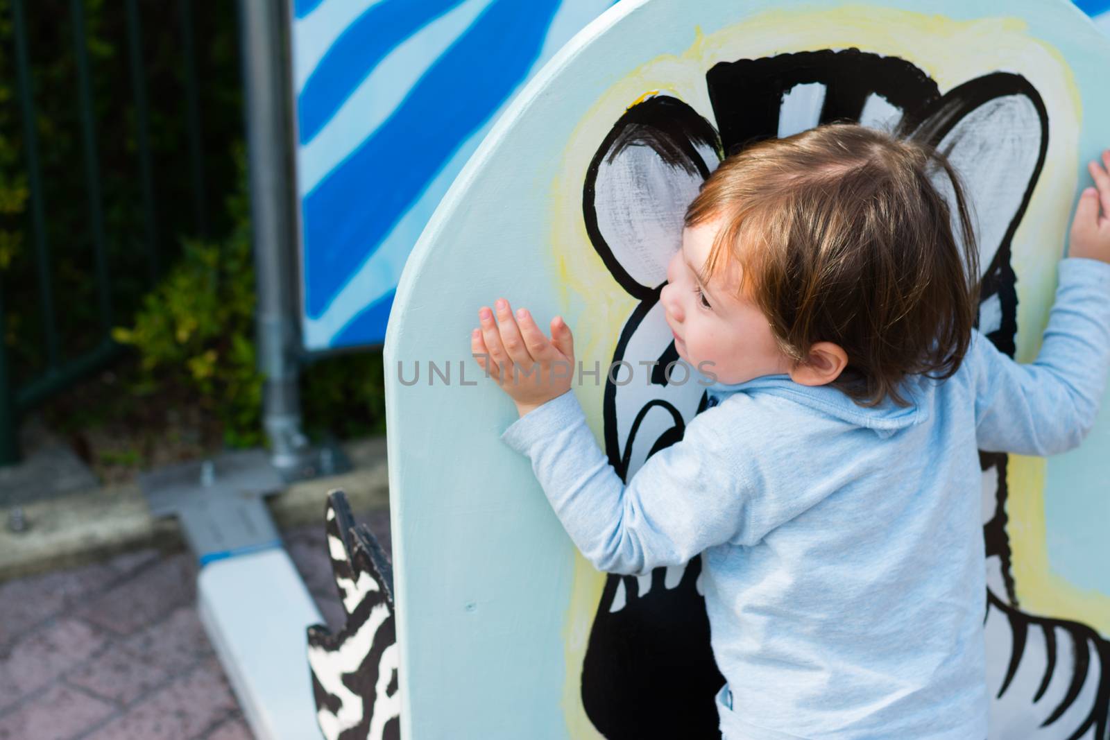 A 2 year old boy hugging a painting of a zebra at a zoo.