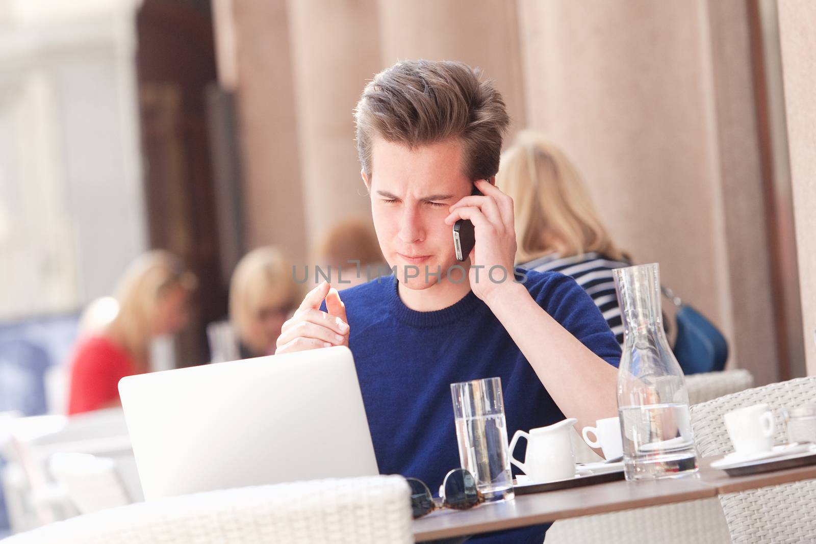 Young Man Sitting in Outside Coffeehouse Talking on Phone by courtyardpix