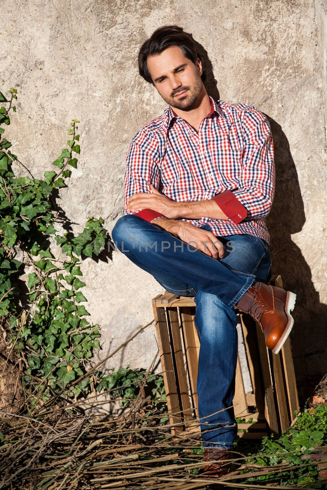Smiling male model sitting on wooden crate with legs crossed