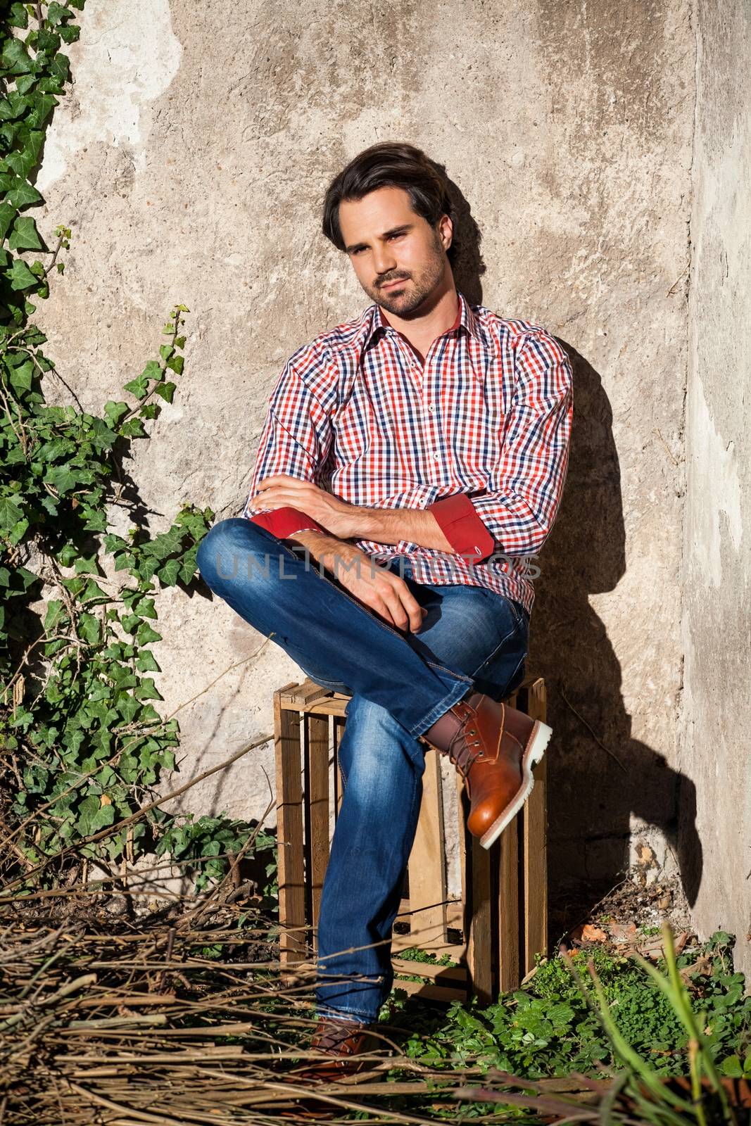 Smiling male model sitting on wooden crate with legs crossed