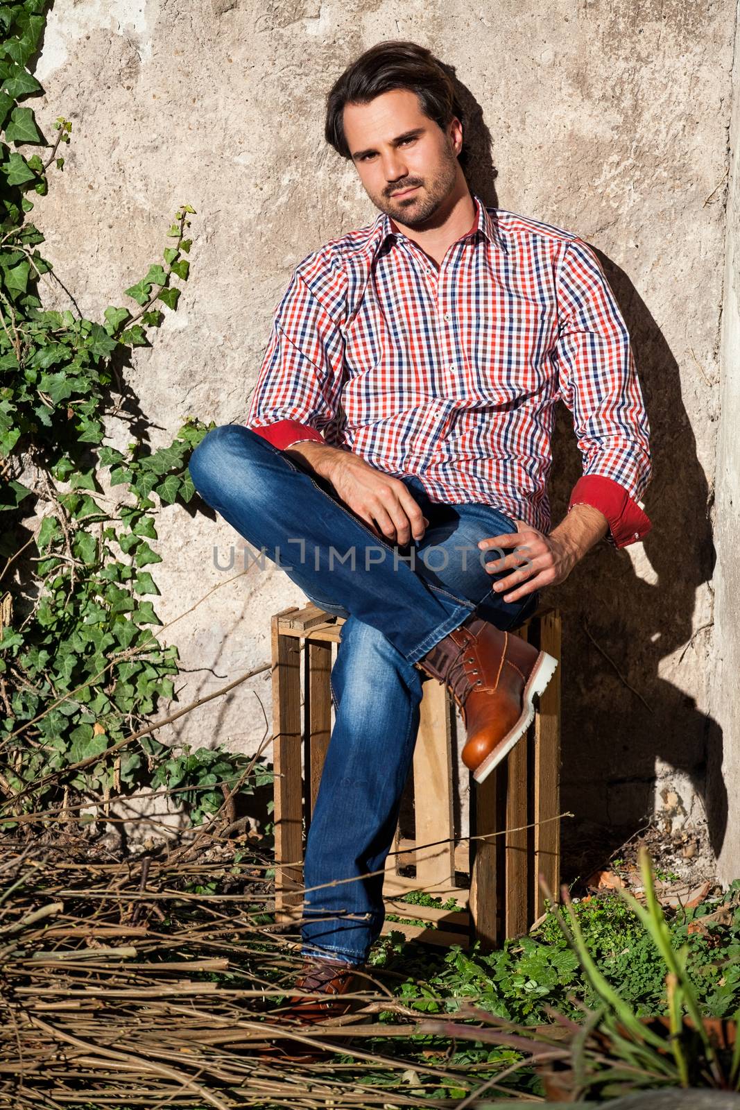 Smiling male model sitting on wooden crate with legs crossed