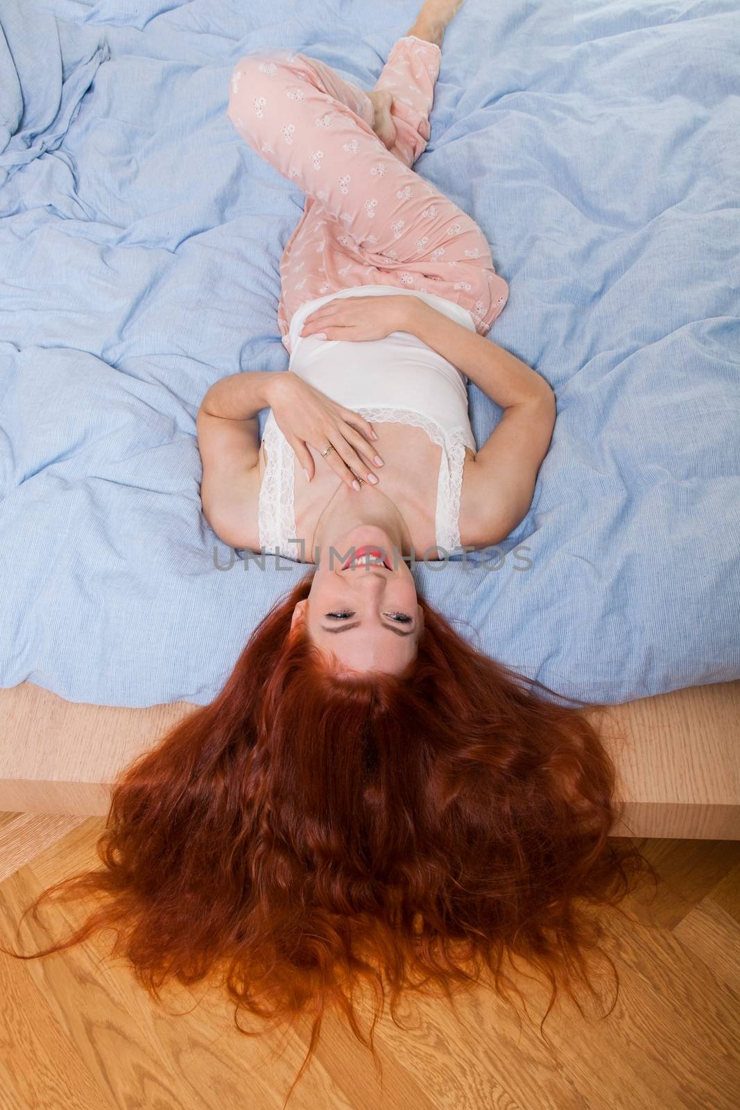 Smiling Pretty Young Woman Lying on her Bed with her Long Blond Hair Hanging Over the Edge, Captured in High Angle View.