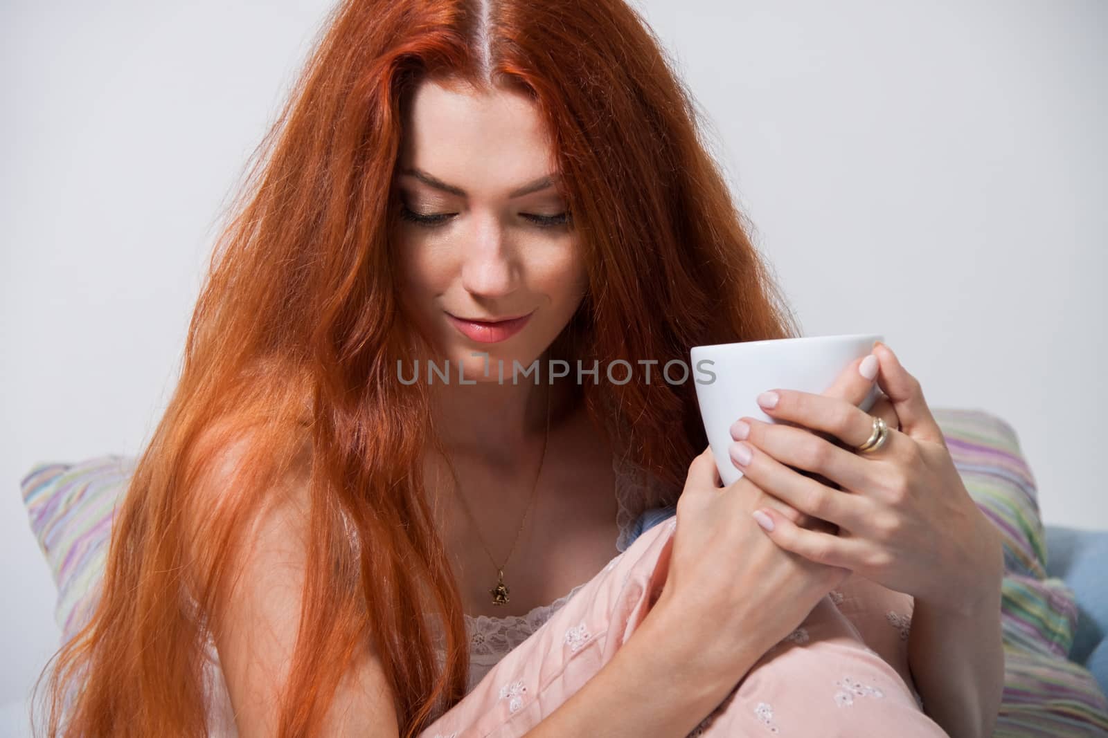 Close up Pensive Blond Woman Holding a White Cup of Coffee While Sitting on her Bed After Waking Up.