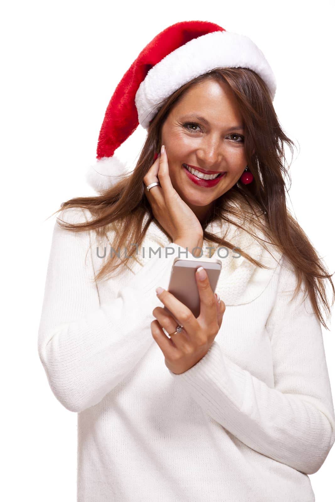 Pretty woman in a Santa hat reading a sms on her mobile phone sending Christmas wishes smiling with pleasure at the news, isolated on white