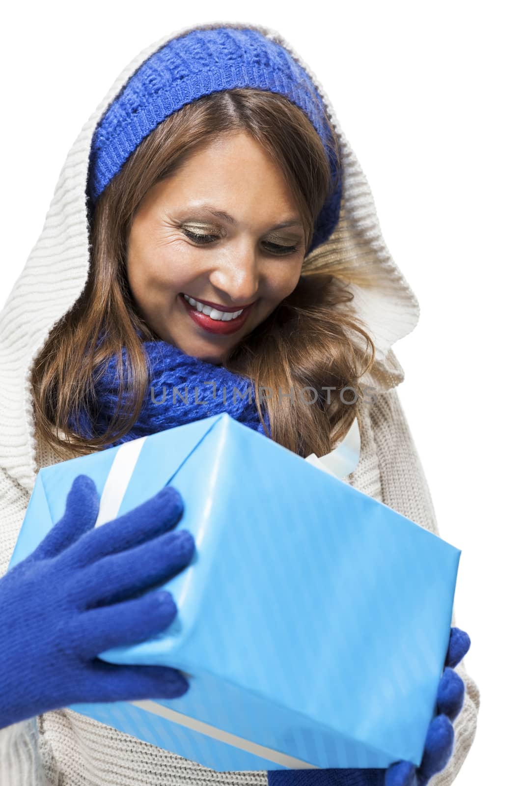 Young woman in fashionable blue knitted winter fashion accessories holding a matching blue gift in her hands looking down at it with a pleased smile, isolated on white