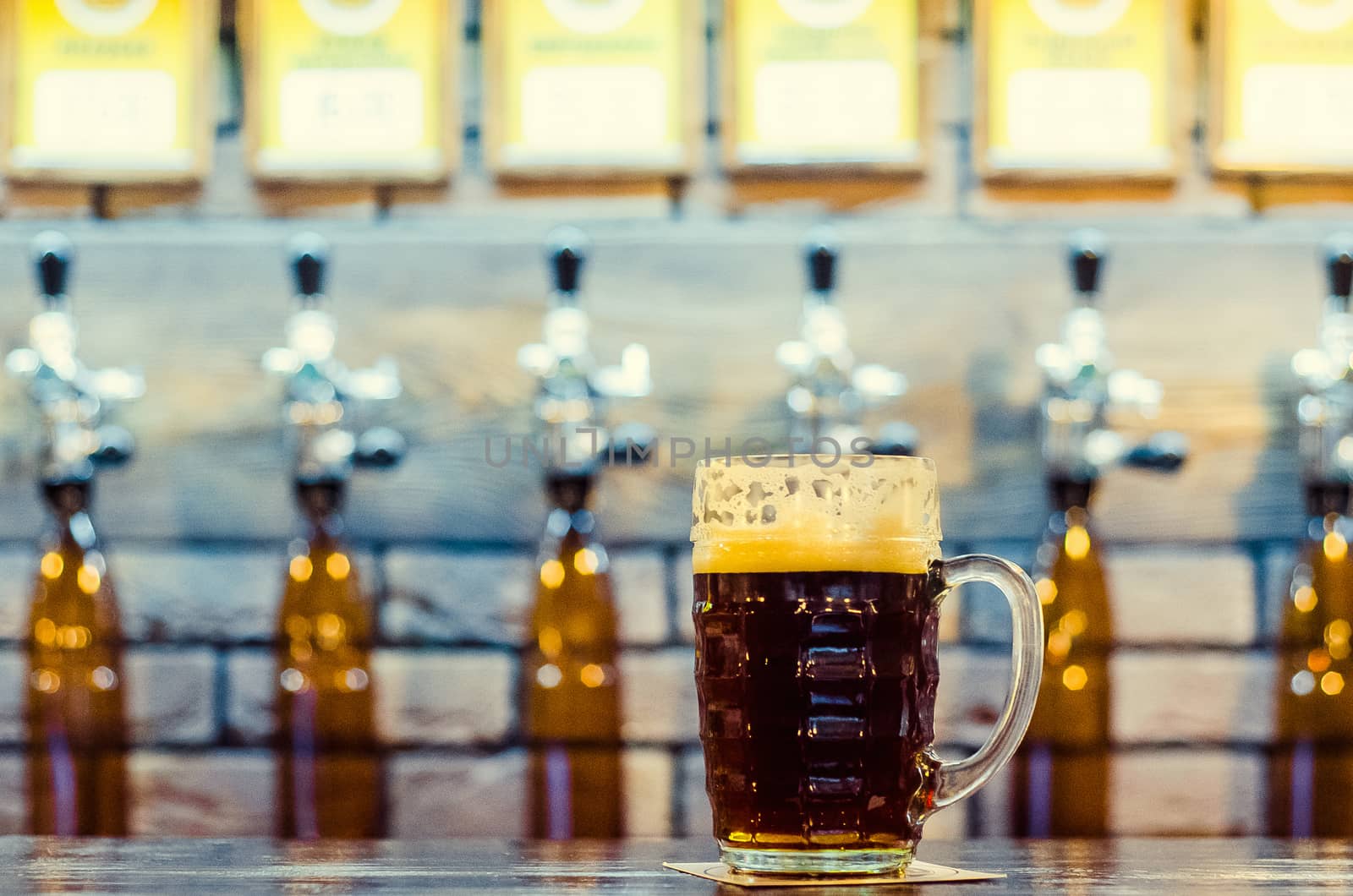 A glass of dark beer on a background of cranes filling beer bottles