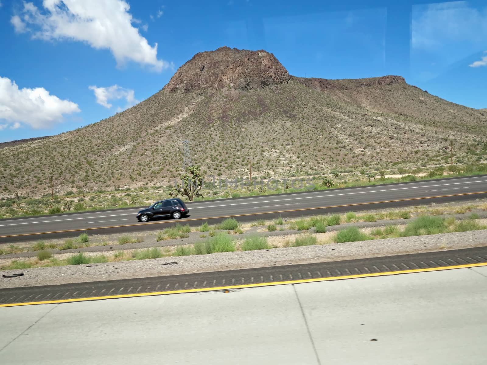 A small mountain along the roadside with car driving by