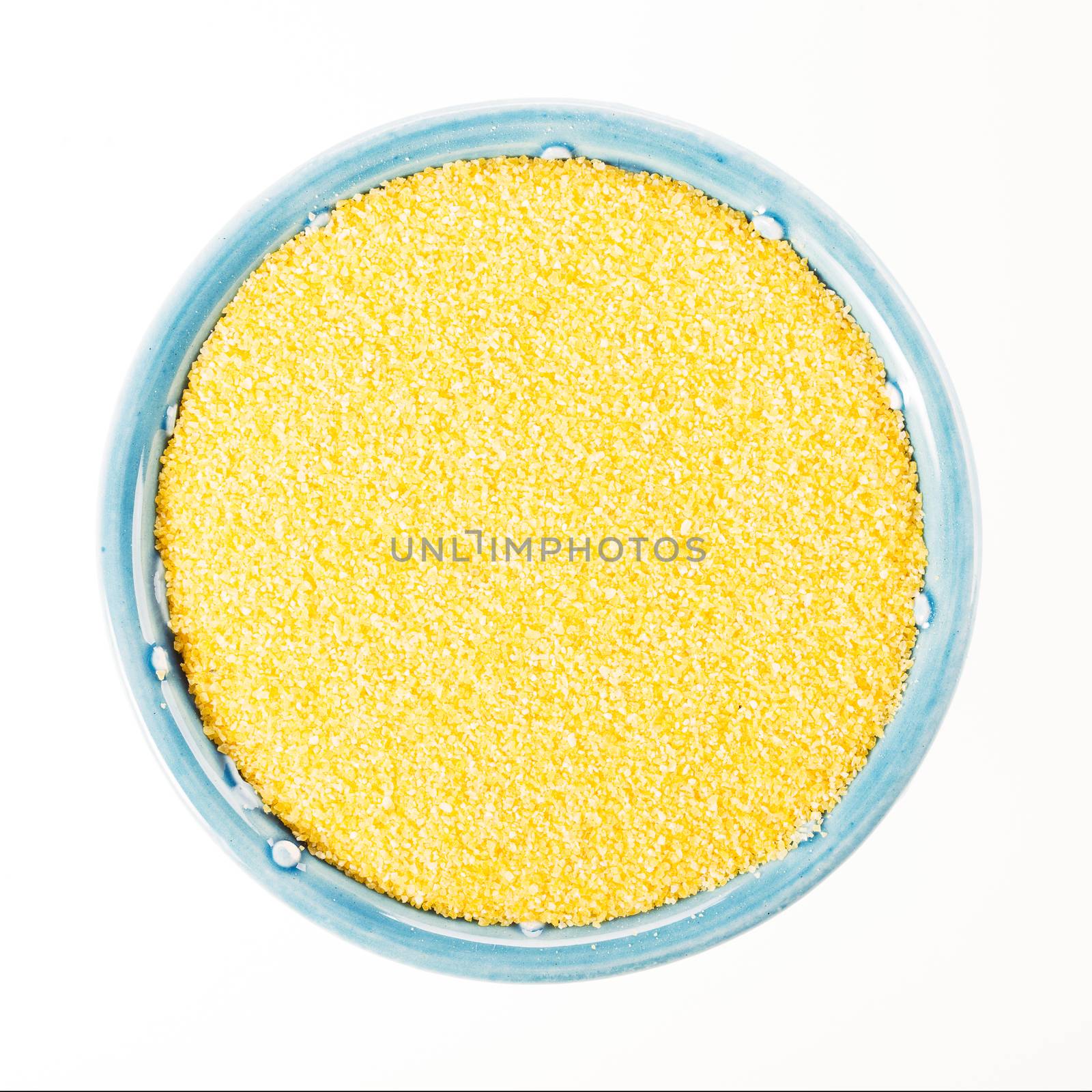 Raw polenta in blue bowl isolated on white background, viewed from directly above.