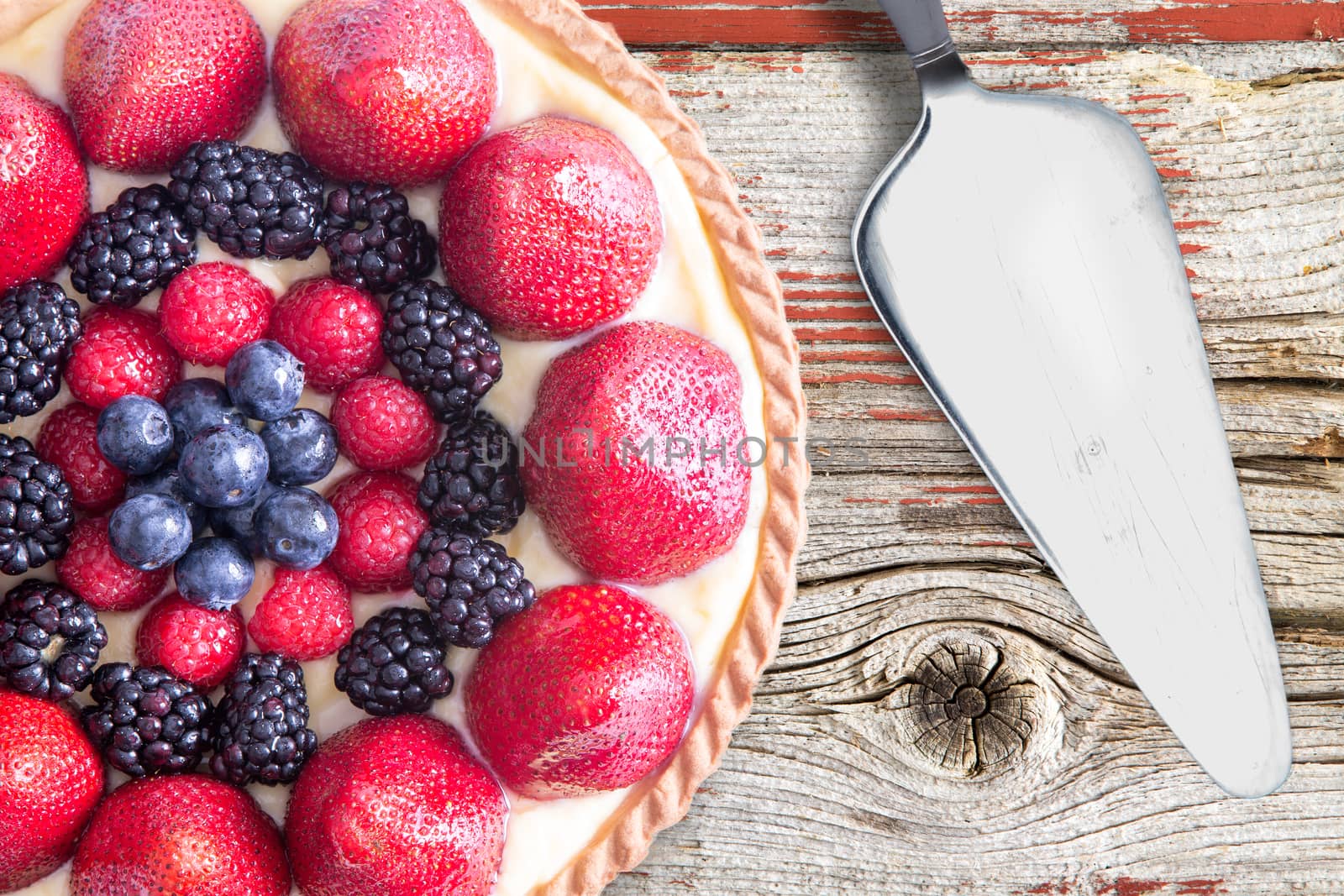 Overhead view of fresh berries homemade tart with spatula, placed on a rustic wooden table.