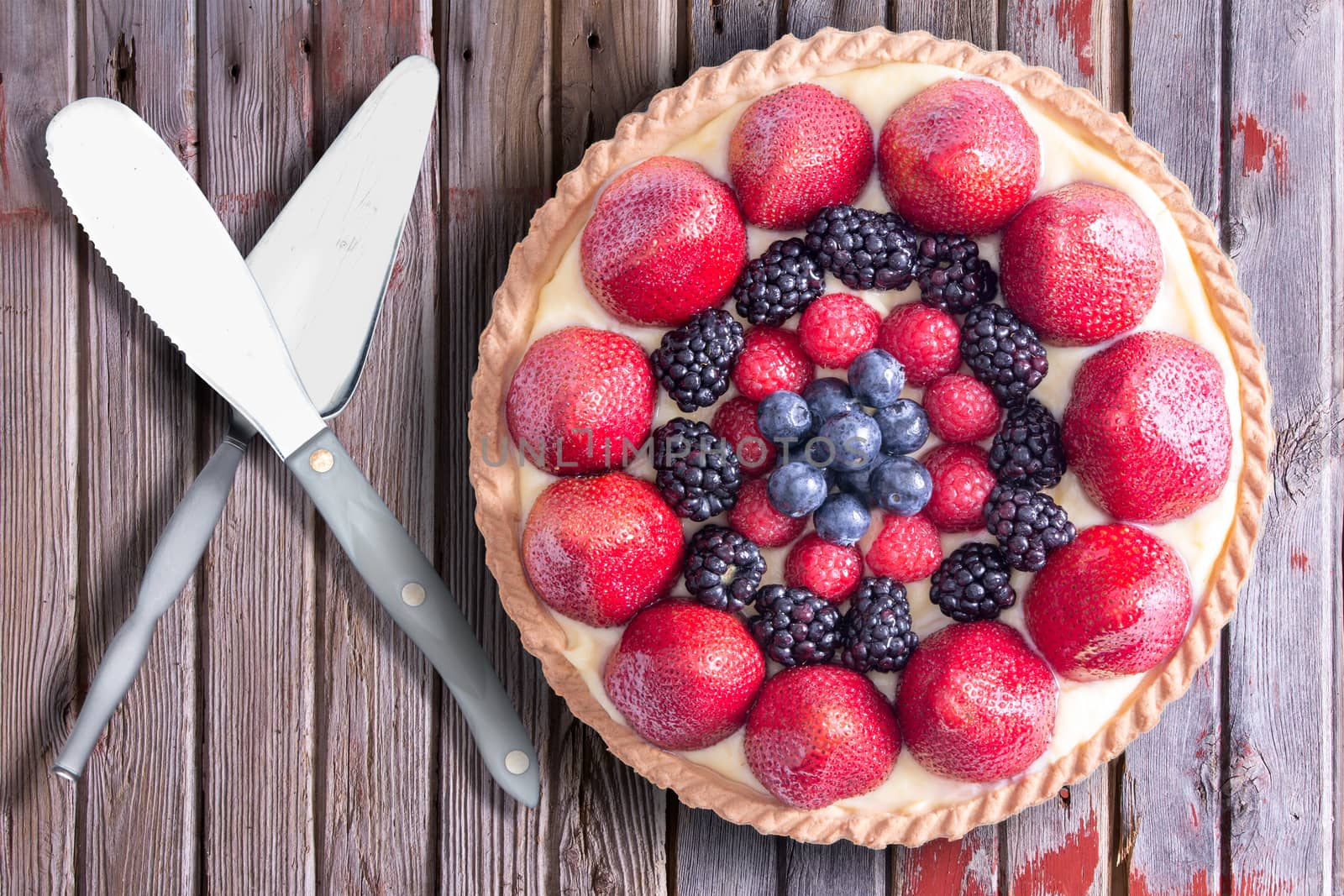 Fresh berries homemade tart with serving utensils, placed on a rustic wooden table. Above view.