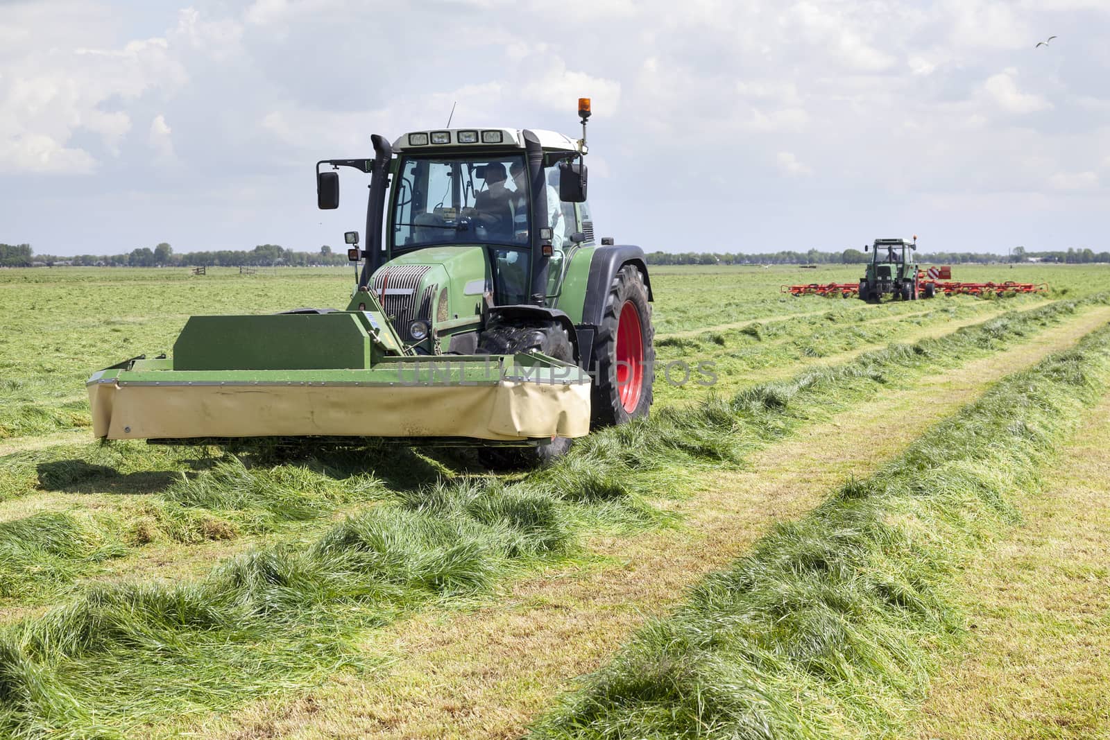 tractor and mower in green meadow in the netherlands on sunny day