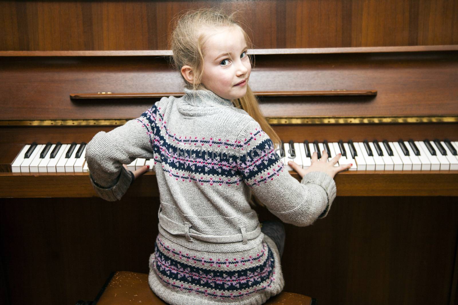 young girl sits at brown  upright piano by ahavelaar