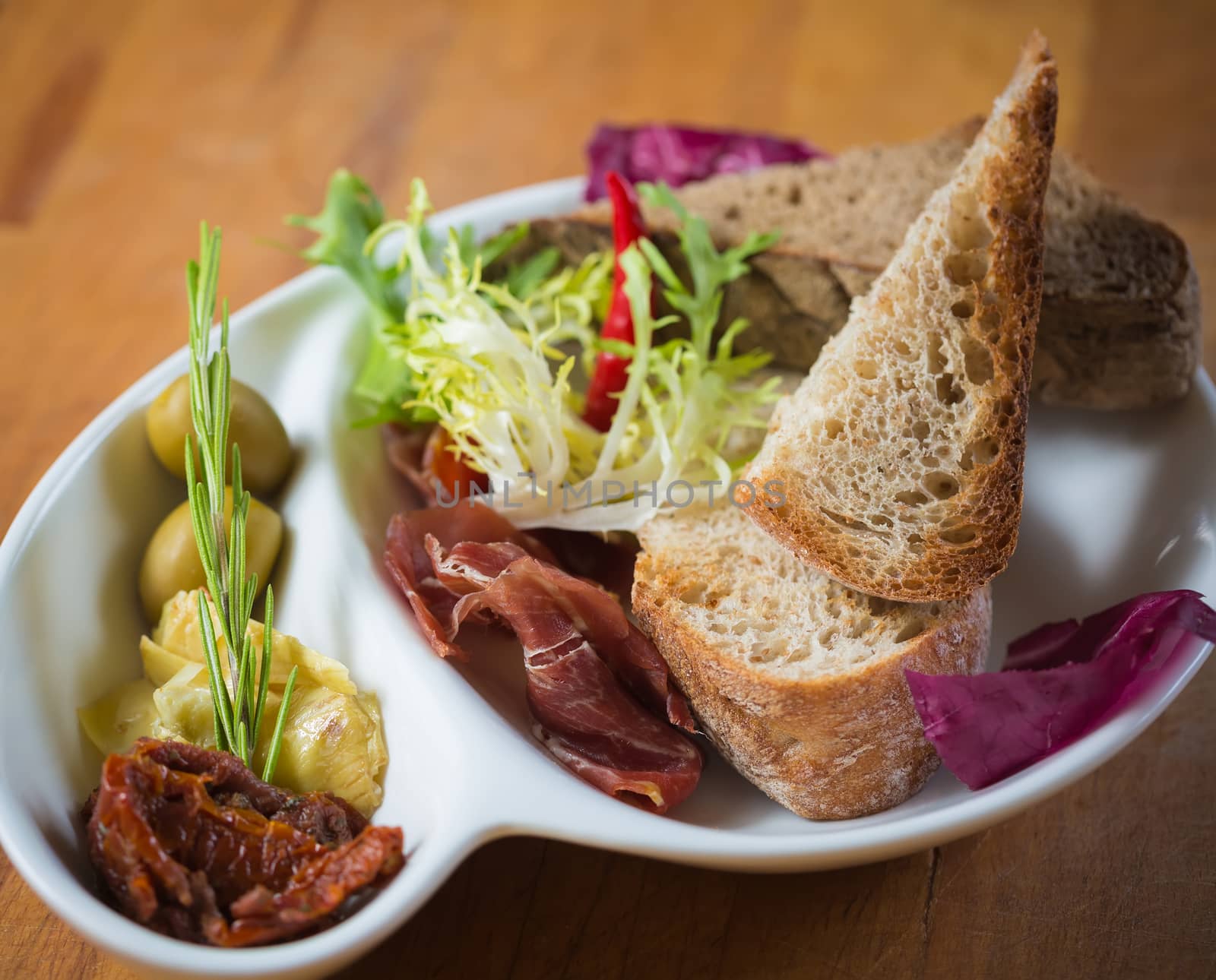 Antipasto. Dried tomatoes, olives, prosciutto and bread in a white plate. Shallow dof