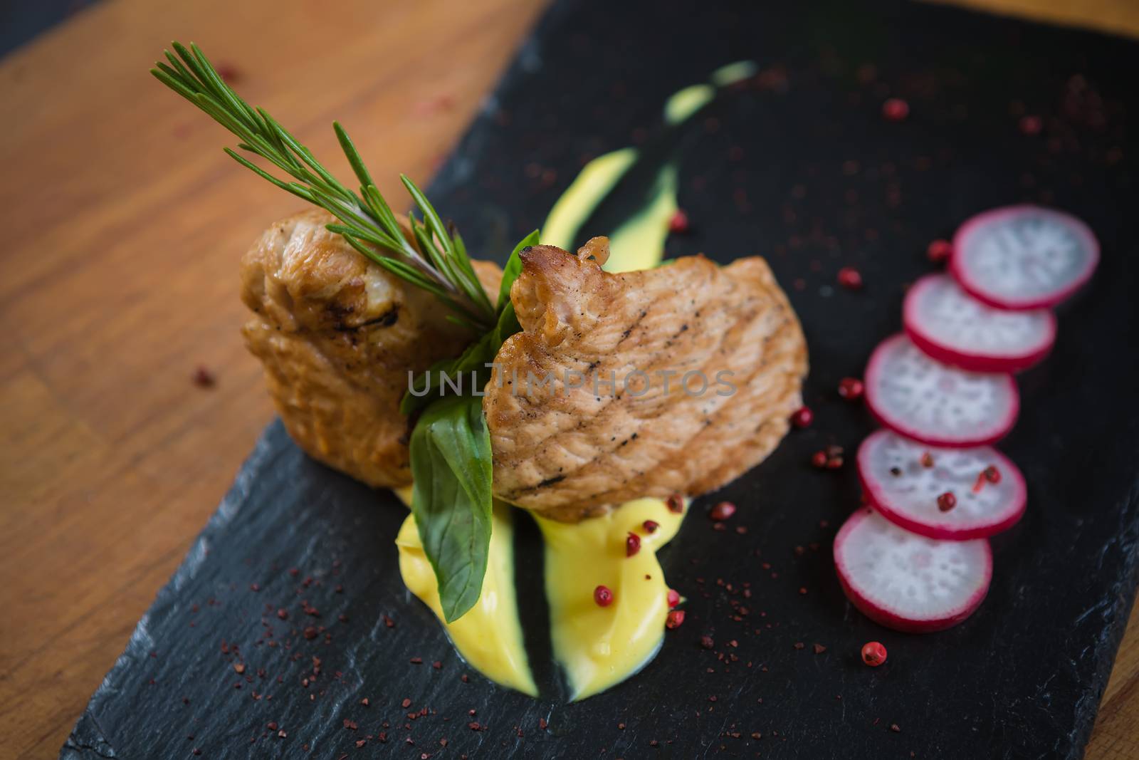 Grilled turkey steak on black board and brown wooden background