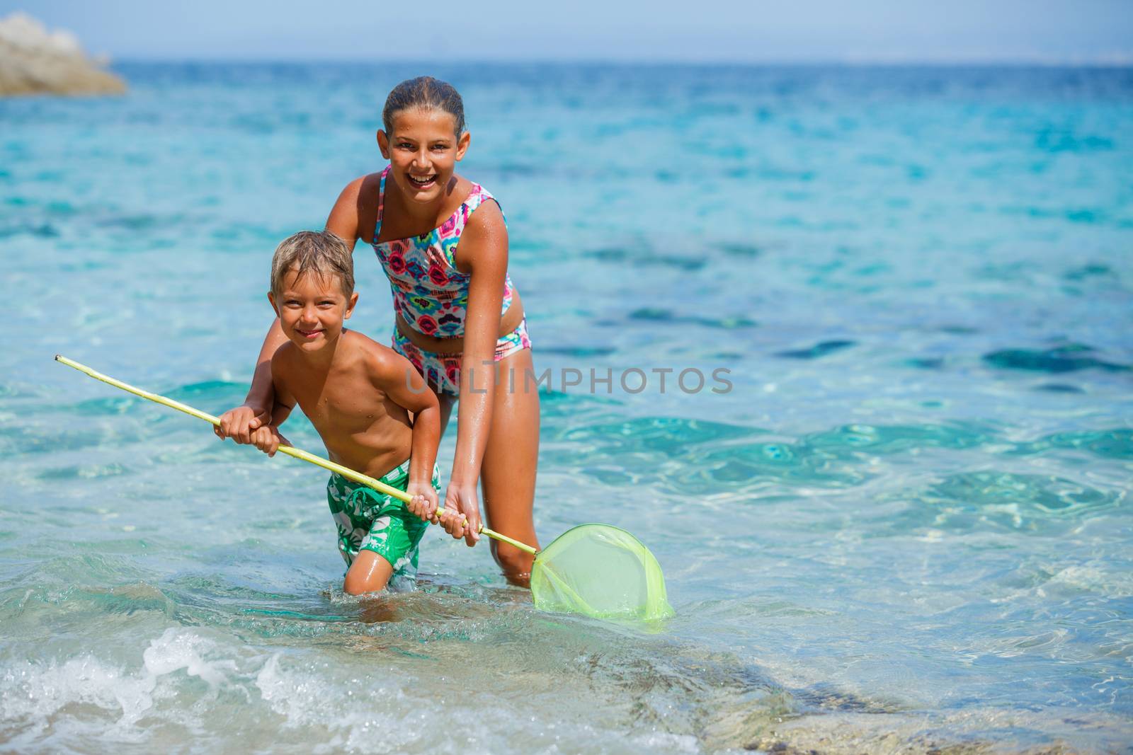 Cute boy and his sister playing with scoop-net and swimming in the transparent sea