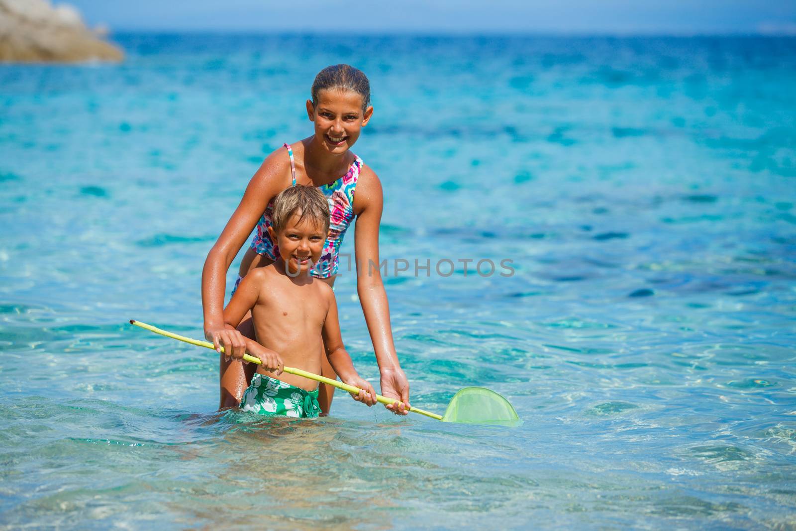 Cute boy and his sister playing with scoop-net and swimming in the transparent sea