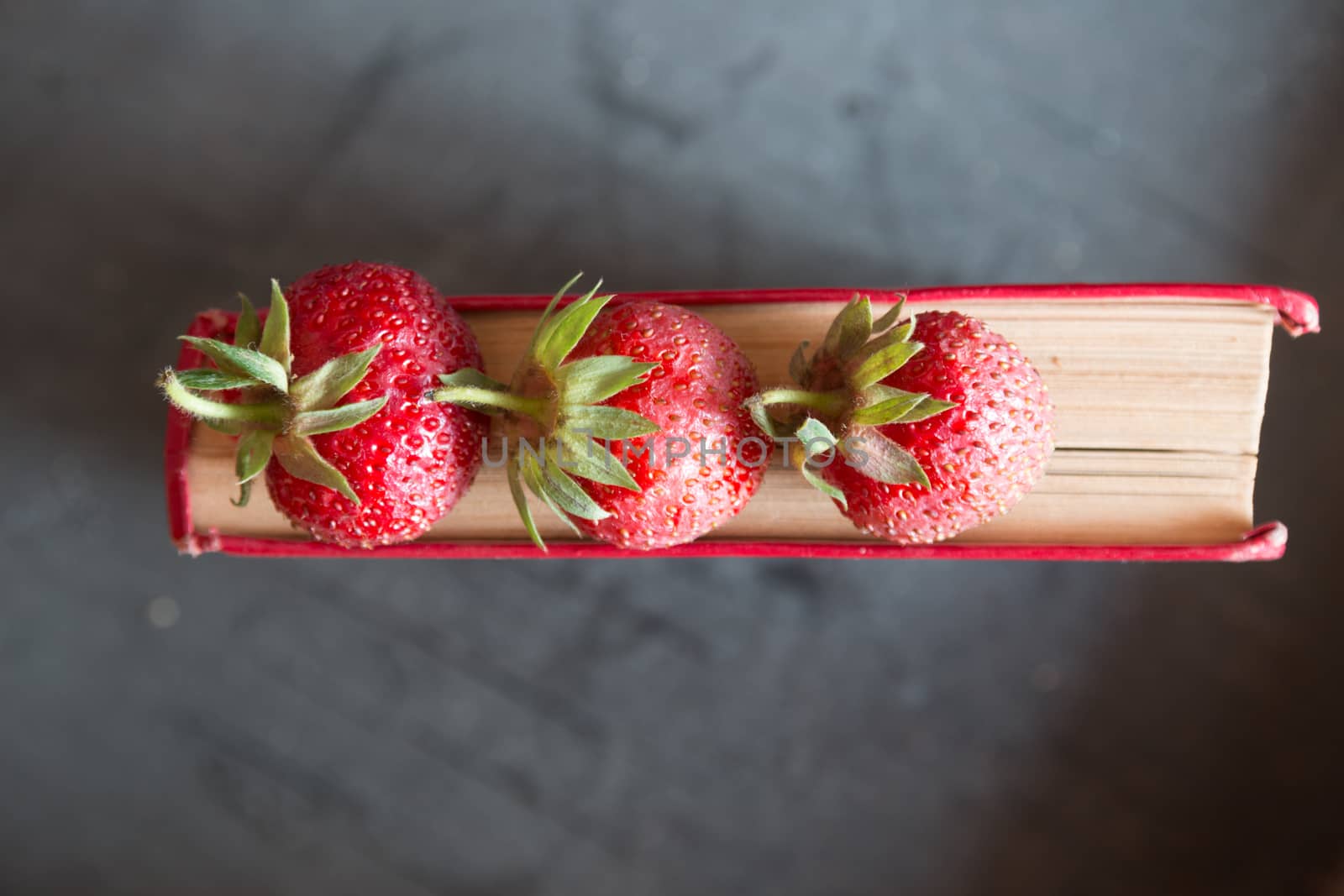 Strawberries and  red cook book on a dark table