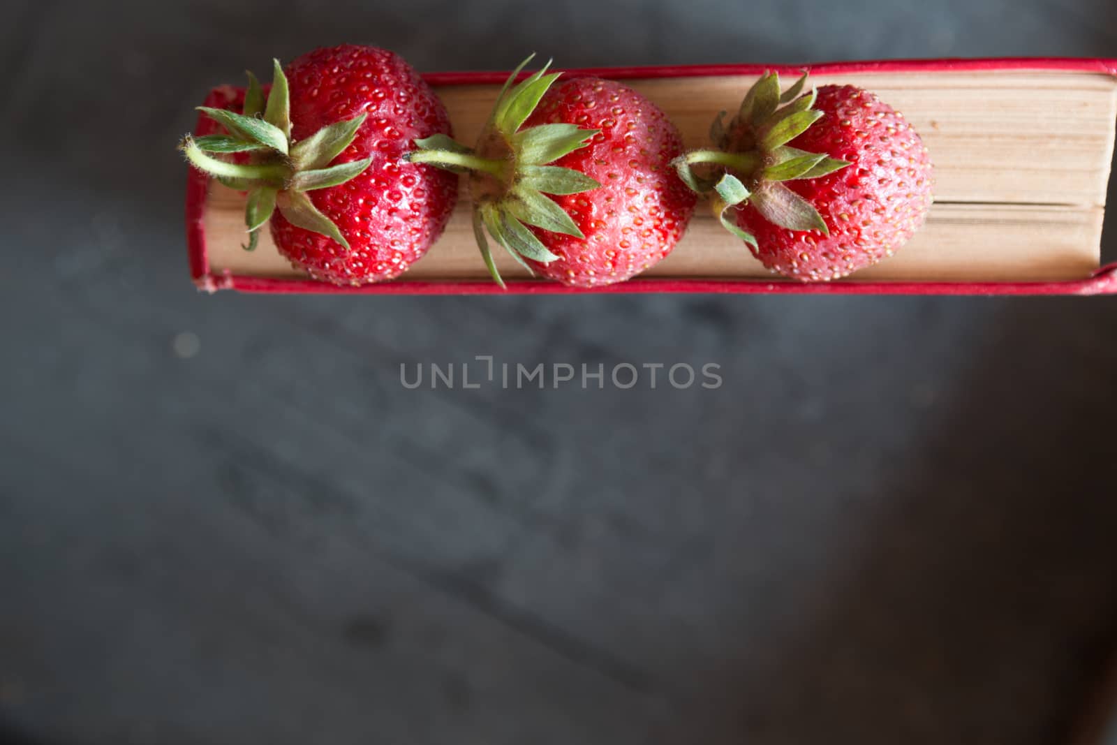 Strawberries and  red cook book on a dark table